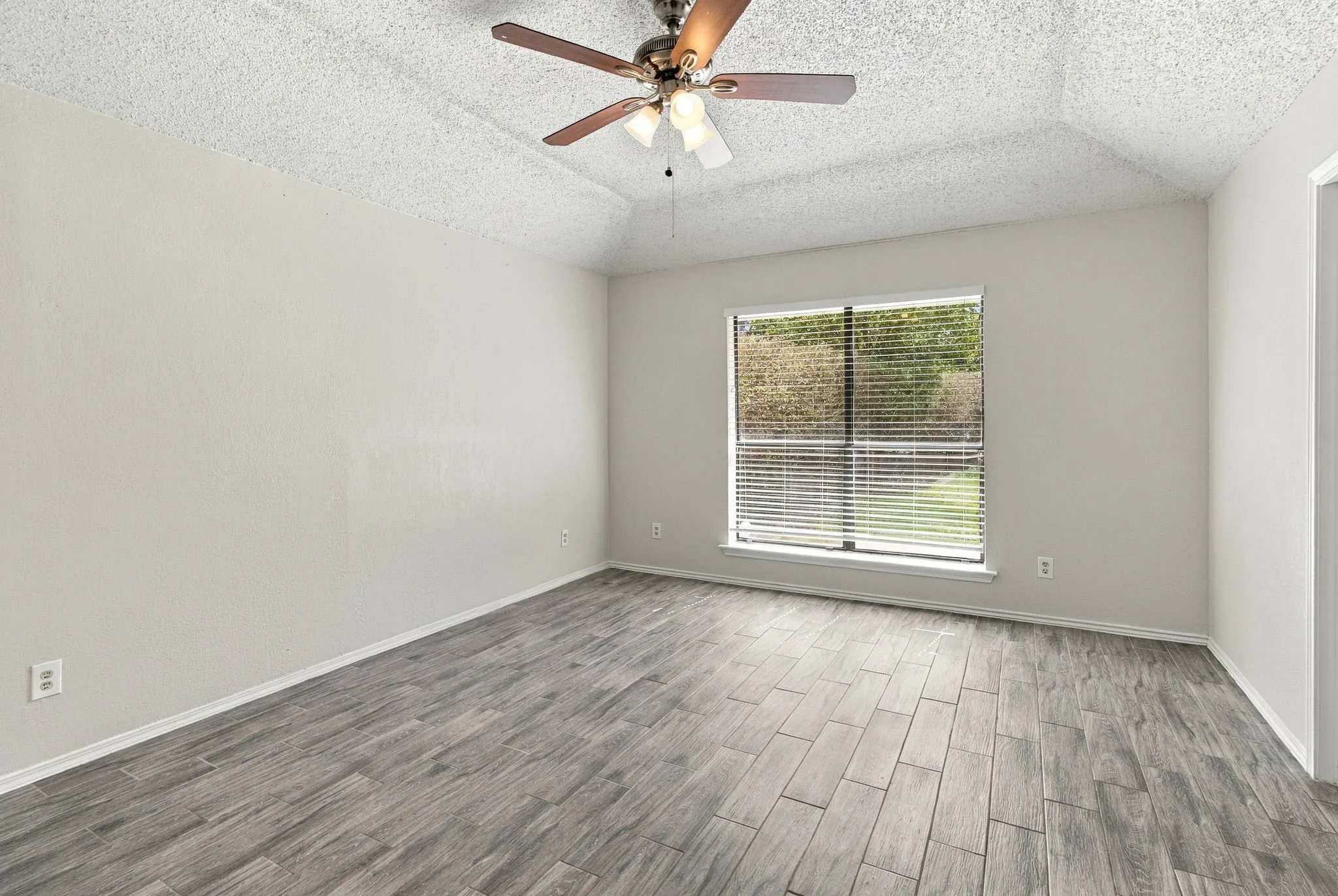 Room featuring a tray ceiling, wood-finish tile flooring, a central ceiling fan with integrated lighting, and a single-pane window with horizontal blinds