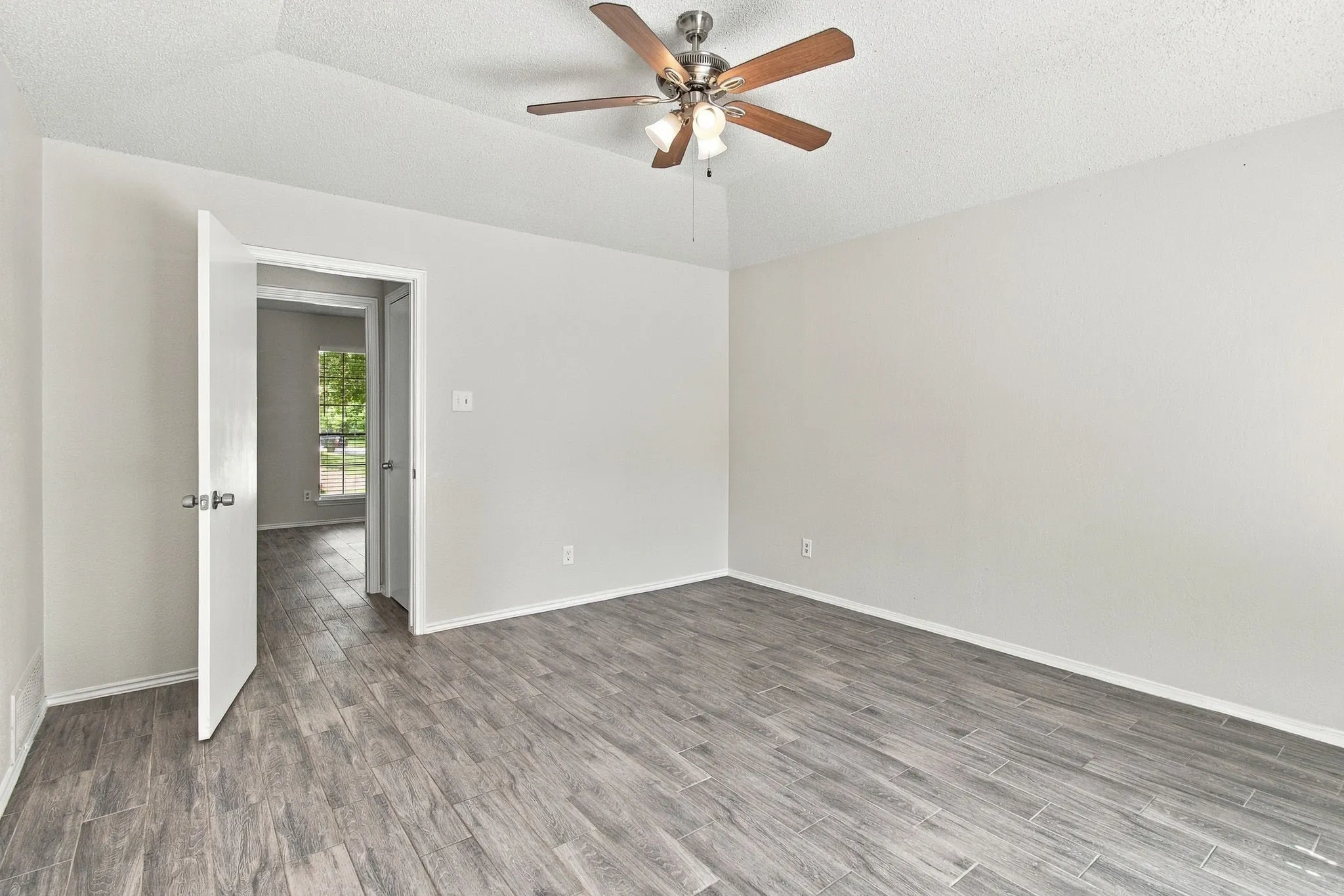 Neutral-toned room featuring tray ceiling, wood-finish flooring, and ceiling fan with integrated lighting