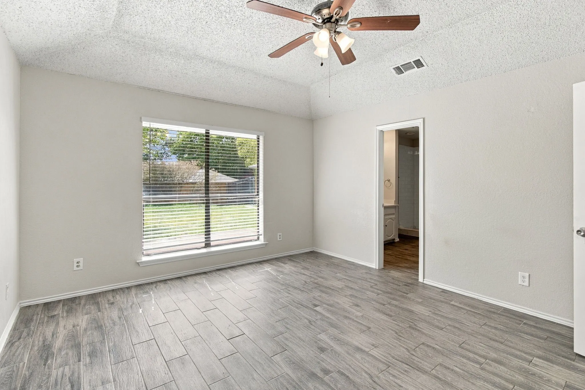 Room featuring wood-finish flooring, a tray ceiling, ceiling fan with integrated lighting, and a window with horizontal blinds