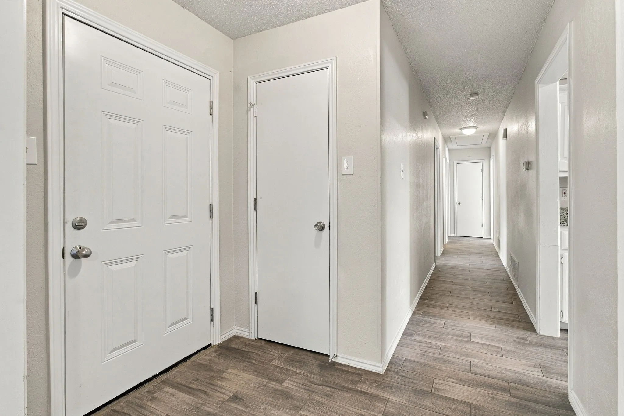 Entryway featuring a six-panel exterior door, neutral wall finishes, and wood-finish flooring extending throughout the hallway