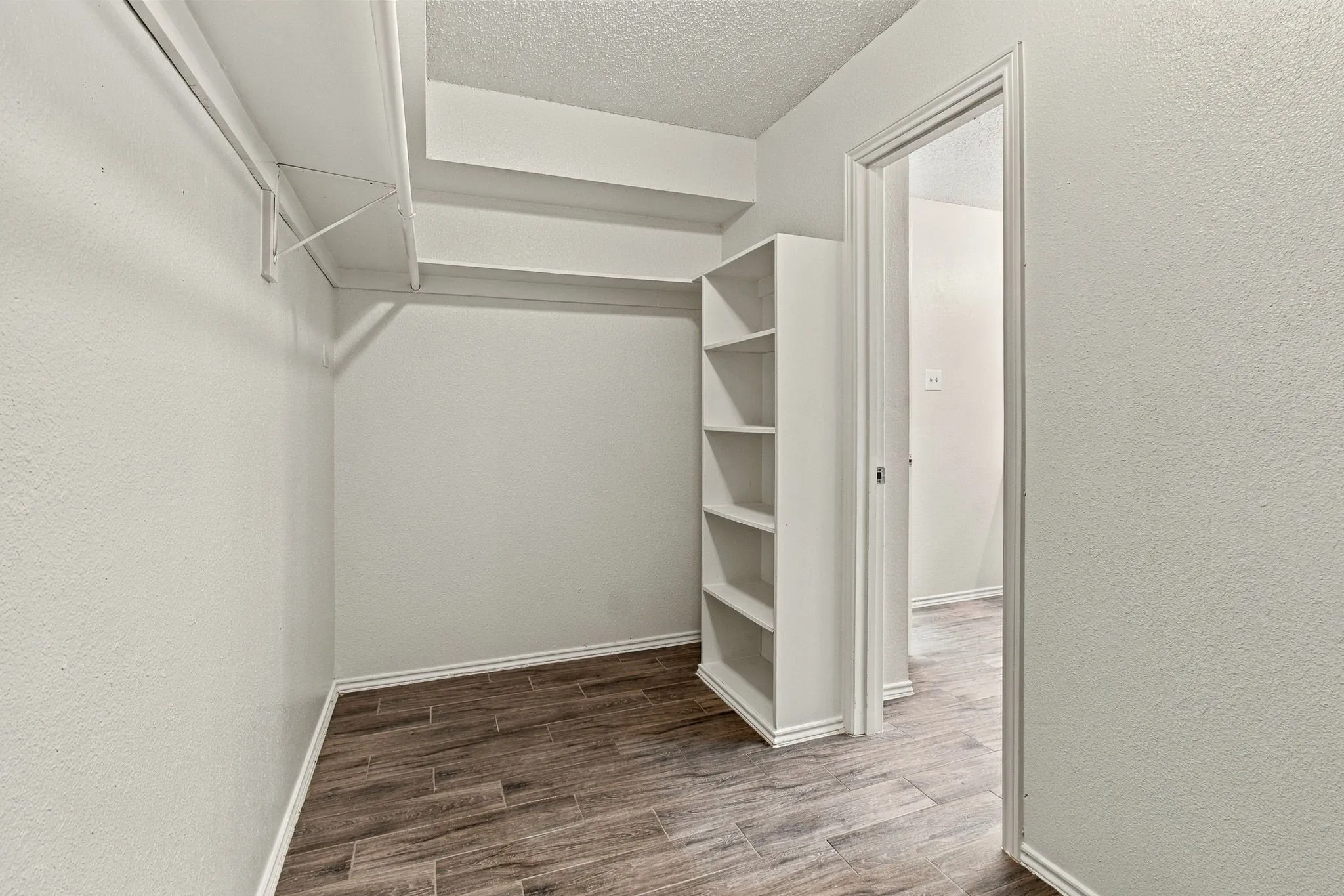 Walk-in closet featuring wood-finish flooring, built-in shelving unit, and overhead shelving rods
