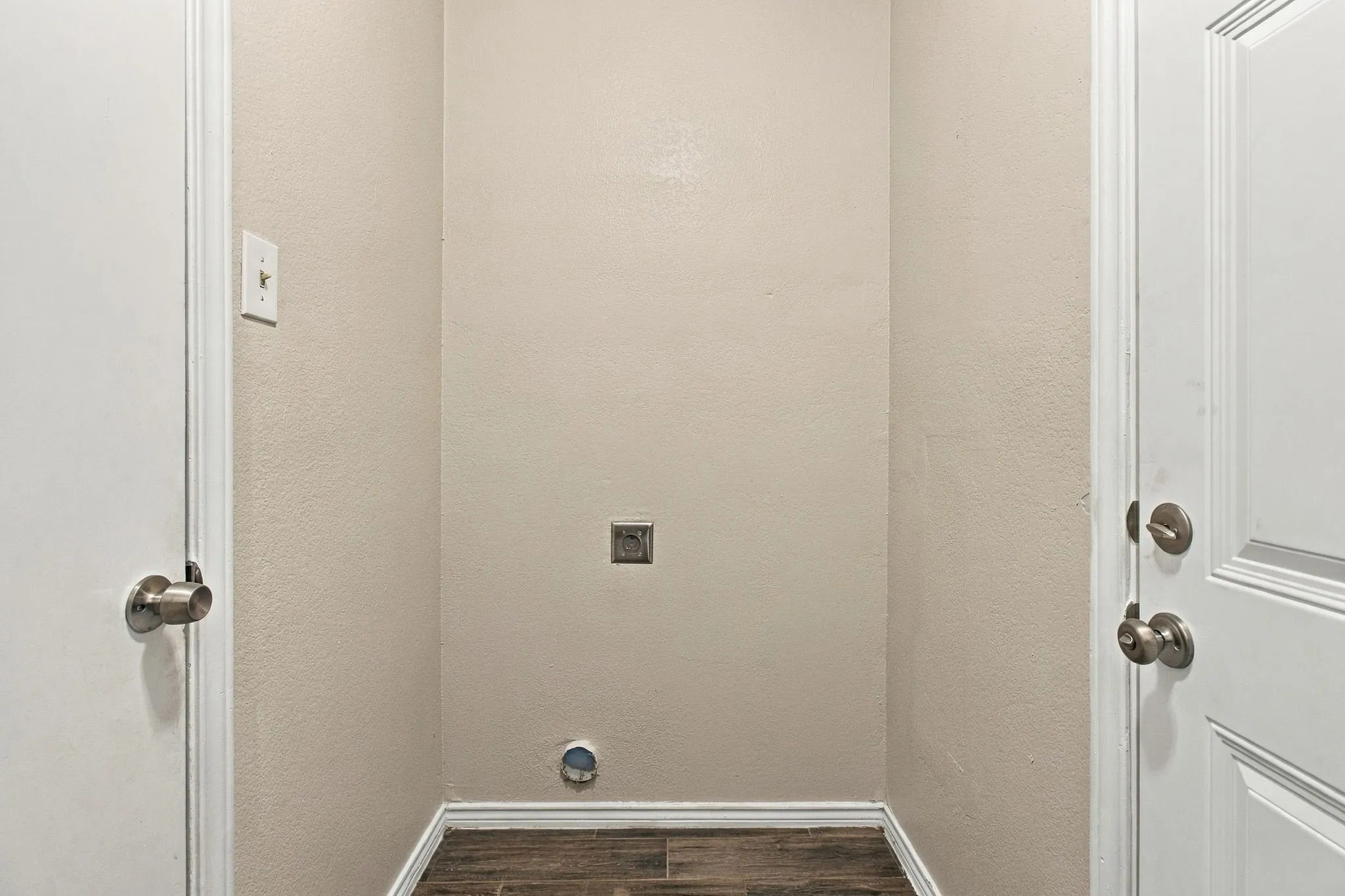 Dedicated utility alcove featuring wood-finish flooring, textured walls, and integrated plumbing connections