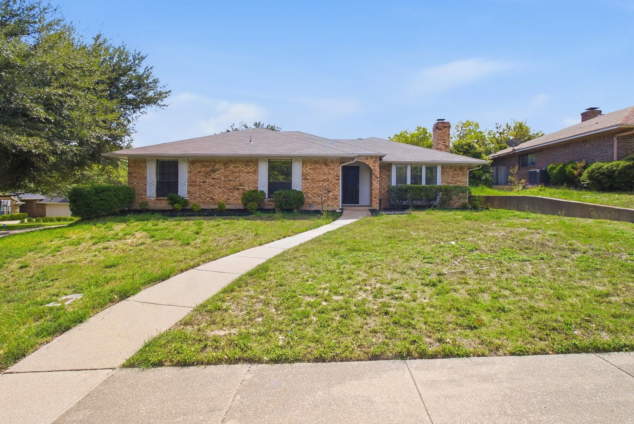 Brick exterior featuring an arched entryway, masonry chimney, and concrete walkway
