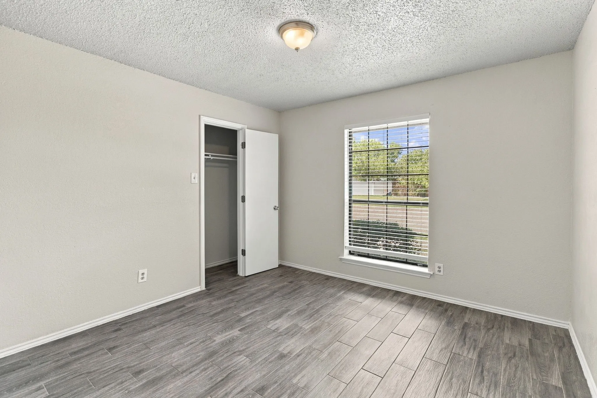 Neutral-toned walls, wood-finish tile flooring, a walk-in closet with integrated shelving, and a dual-pane window with horizontal blinds