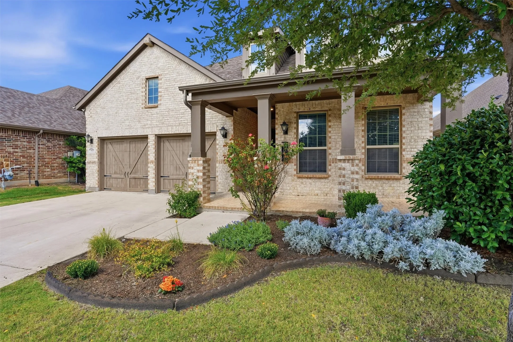 Up-close view of the covered entryway highlighting stone-accented support columns and vibrant flower beds.