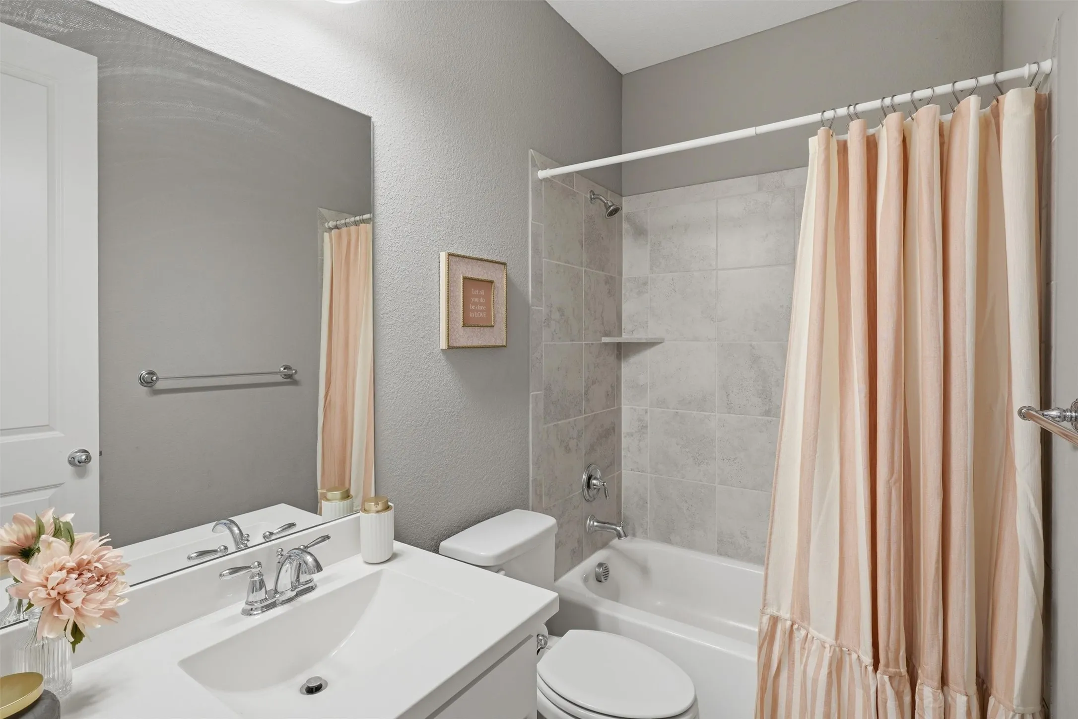 Full secondary bathroom featuring a tub-and-shower combination with tiled surround, a white vanity with updated fixtures, and neutral gray walls. Ideal for family or guests with a functional, low-maintenance layout