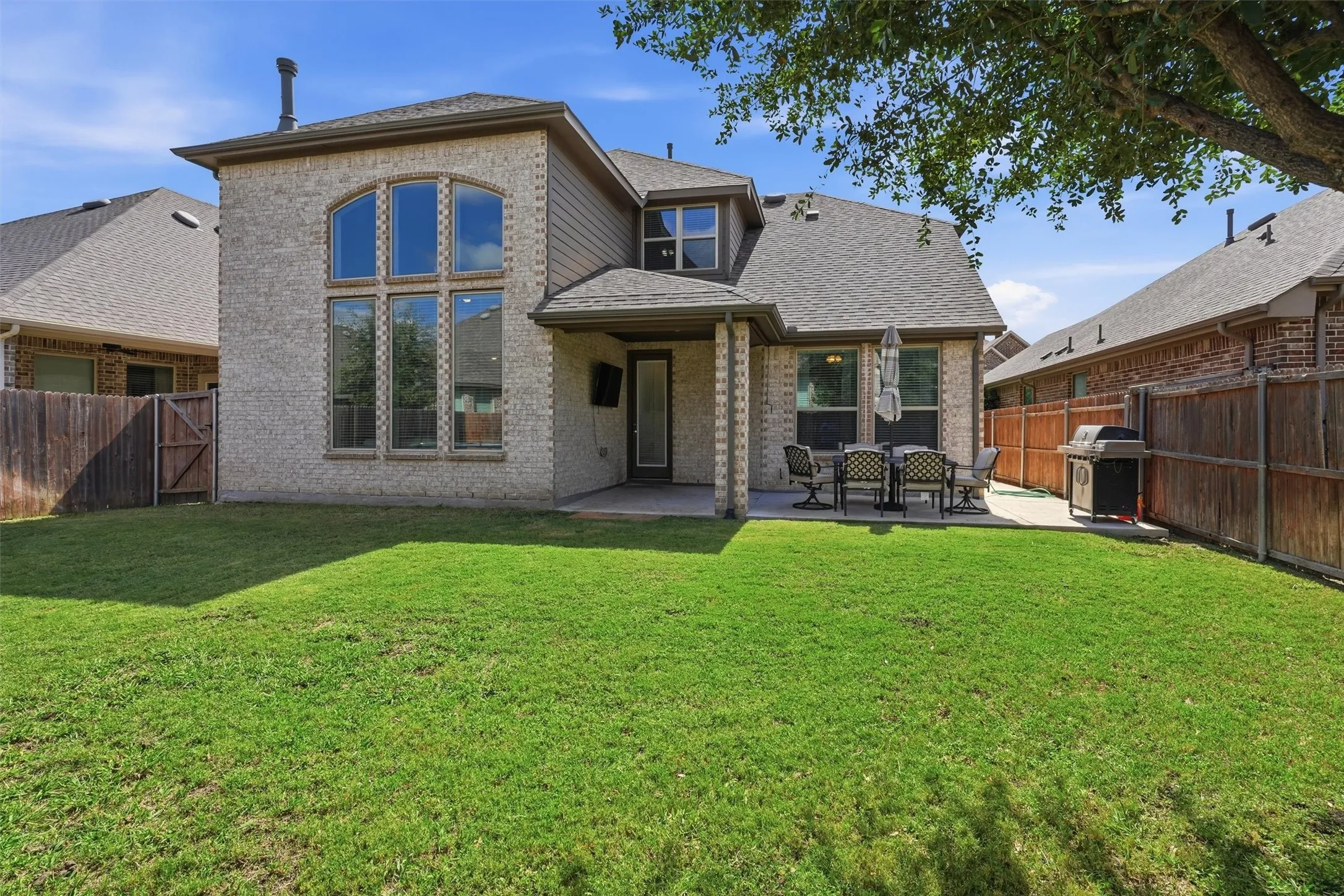 Full rear perspective highlighting the expansive, level lawn and fully fenced perimeter. Features striking brick architecture with floor-to-ceiling windows, alongside the extended patio that creates a perfect layout for outdoor play, hosting, and everyday family enjoyment.