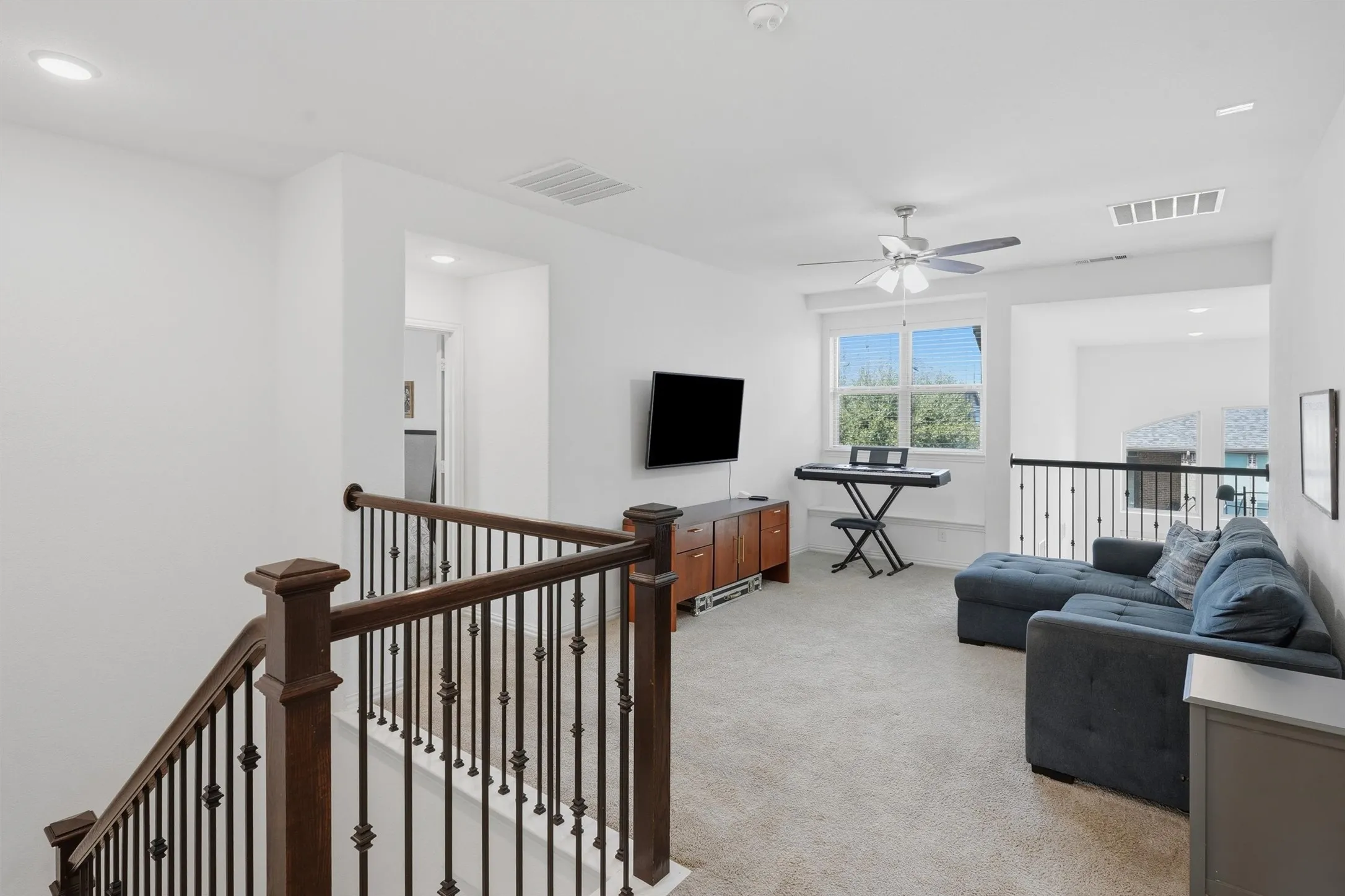 Versatile upstairs game room or loft featuring plush carpeting, wrought-iron stair railing, and a ceiling fan. Open overlook provides a secondary living area ideal for family movie nights, play, or media entertainment