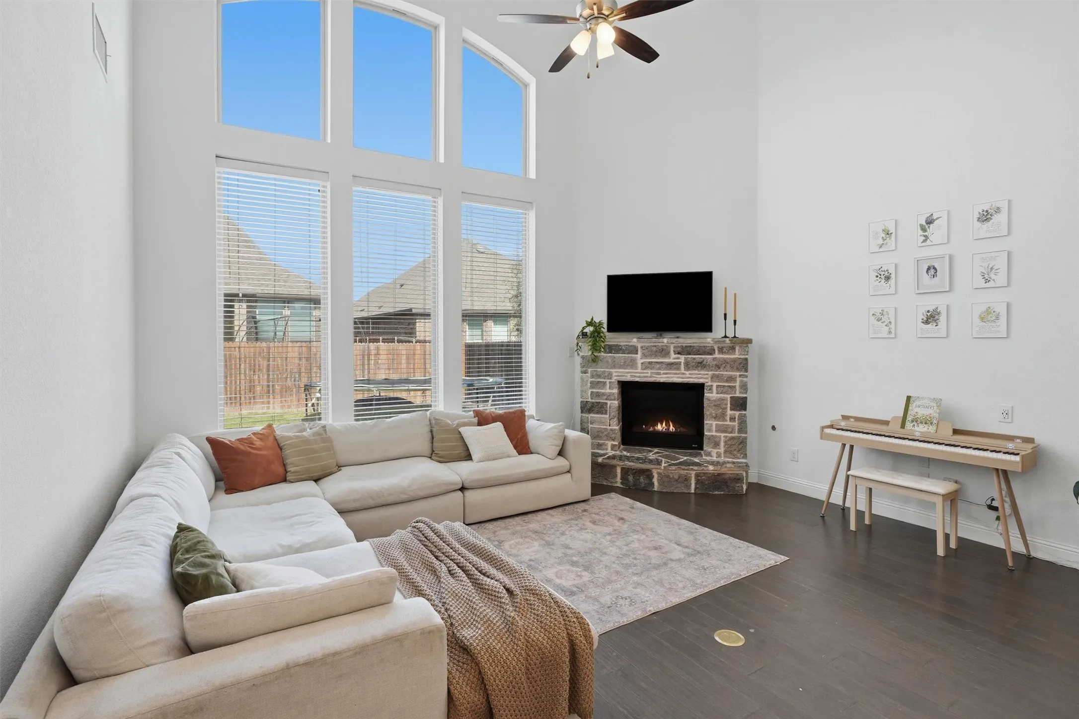 Alternate living room perspective focusing on the floor-to-ceiling arched windows and stacked-stone corner fireplace. Highlights the tall, sunlit walls and dark wood flooring