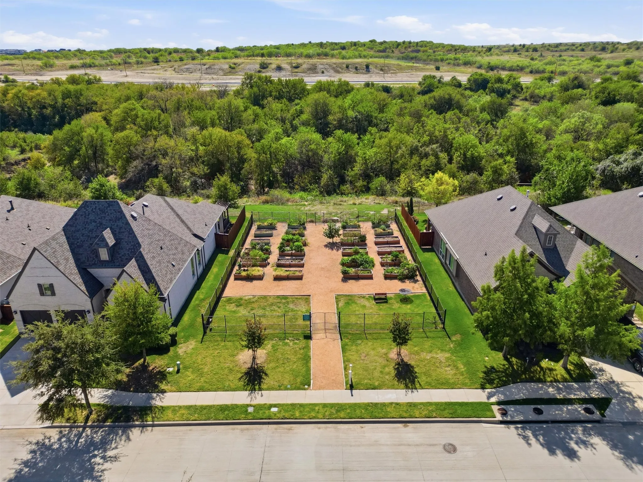 Aerial perspective of the community's dedicated neighborhood garden featuring neatly arranged raised planting beds, gated fencing, and central pathways. Offers residents a shared, green space to cultivate fresh produce, flowers, and herbs while fostering a vibrant sense of community.