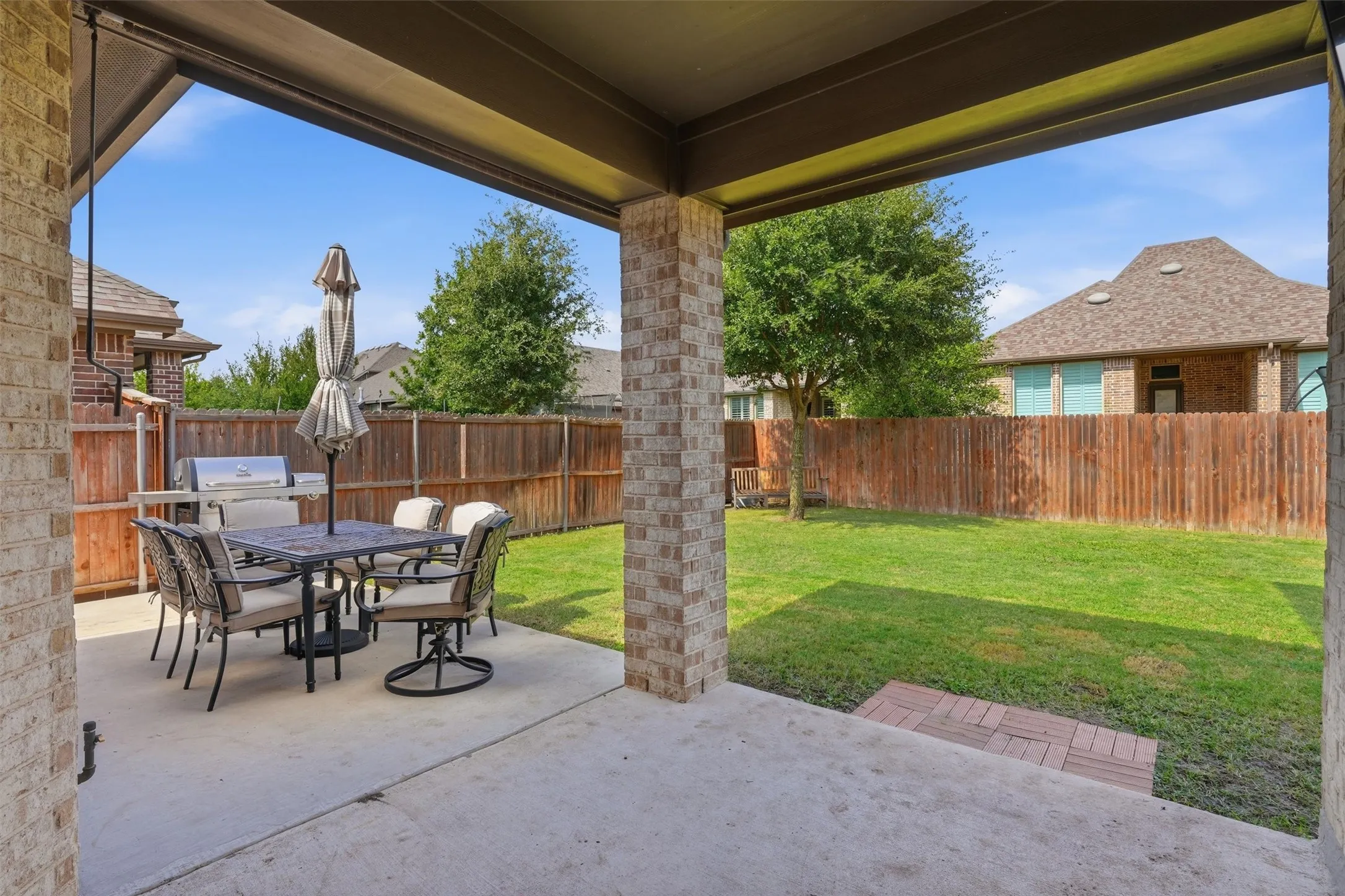 Spacious covered back patio framed by brick support columns, perfect for outdoor dining and entertaining. Opens to a fully fenced, private backyard with a lush green lawn.