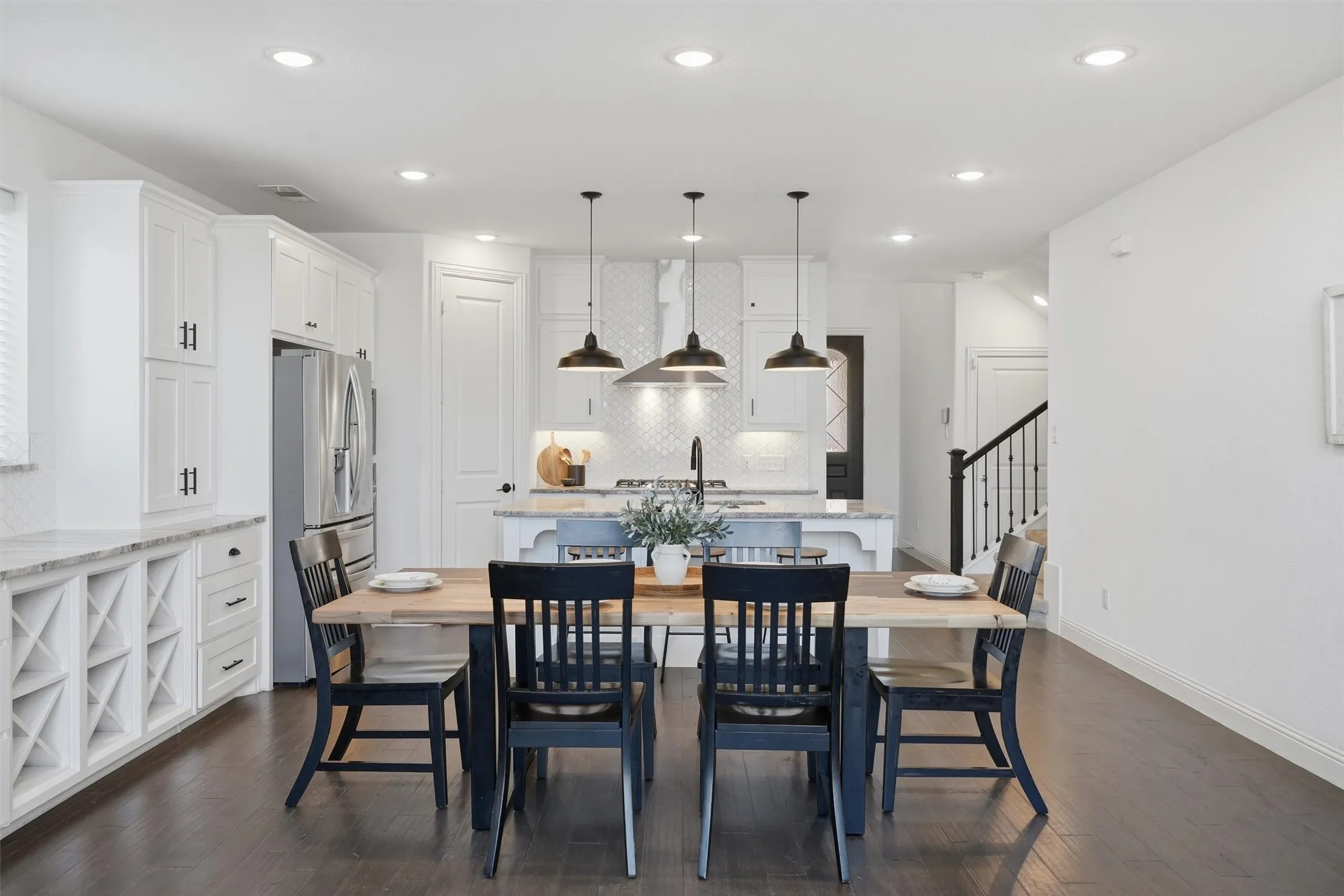 Open concept dining space highlighting the seamless connection to the adjacent kitchen and built-in wine rack cabinetry. Features rich dark wood flooring and bright recessed overhead lighting.