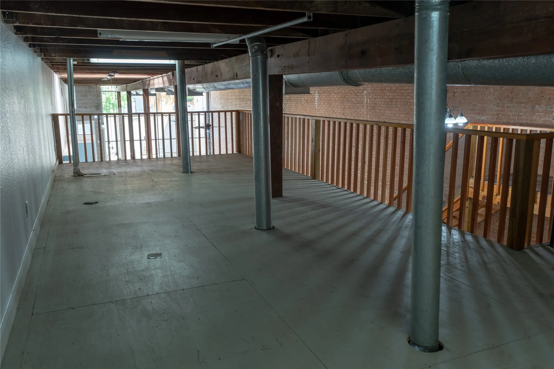 Industrial-style loft space featuring exposed timber beam ceiling, raw brick wall, metallic support columns, and wooden balustrades