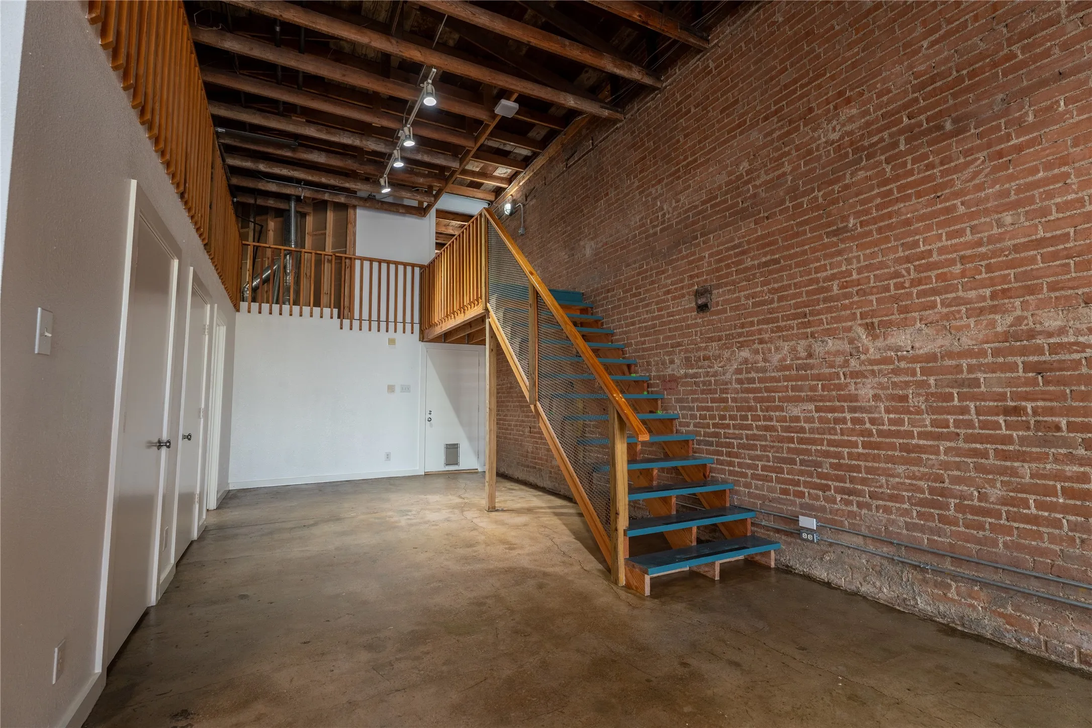Exposed brick wall, polished concrete flooring, open-beam wood ceiling, and custom staircase featuring wood handrails and glass panels