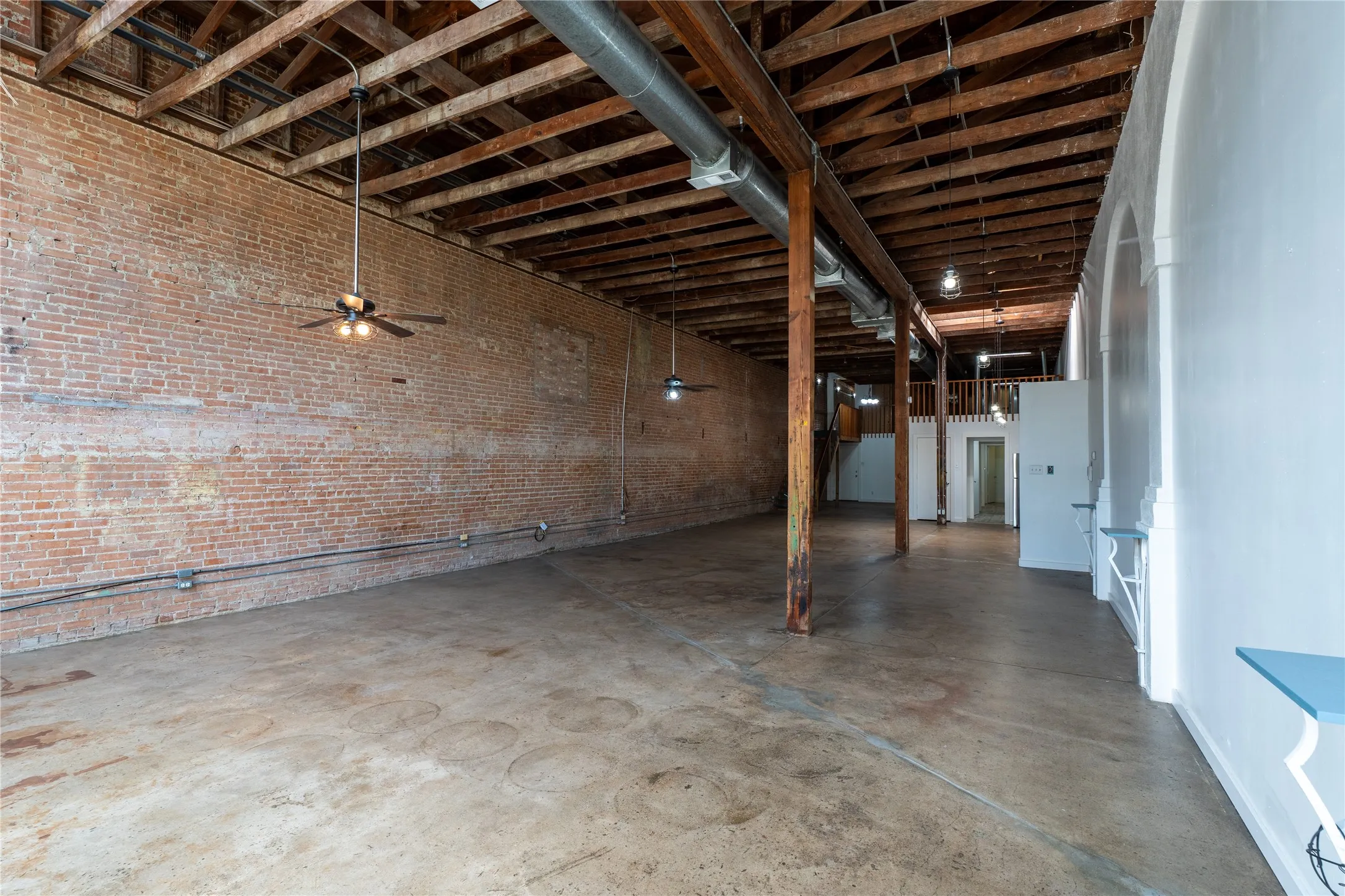 Open interior space featuring exposed brick walls, industrial timber ceiling beams, polished concrete flooring, exposed ductwork, and structural wooden support columns