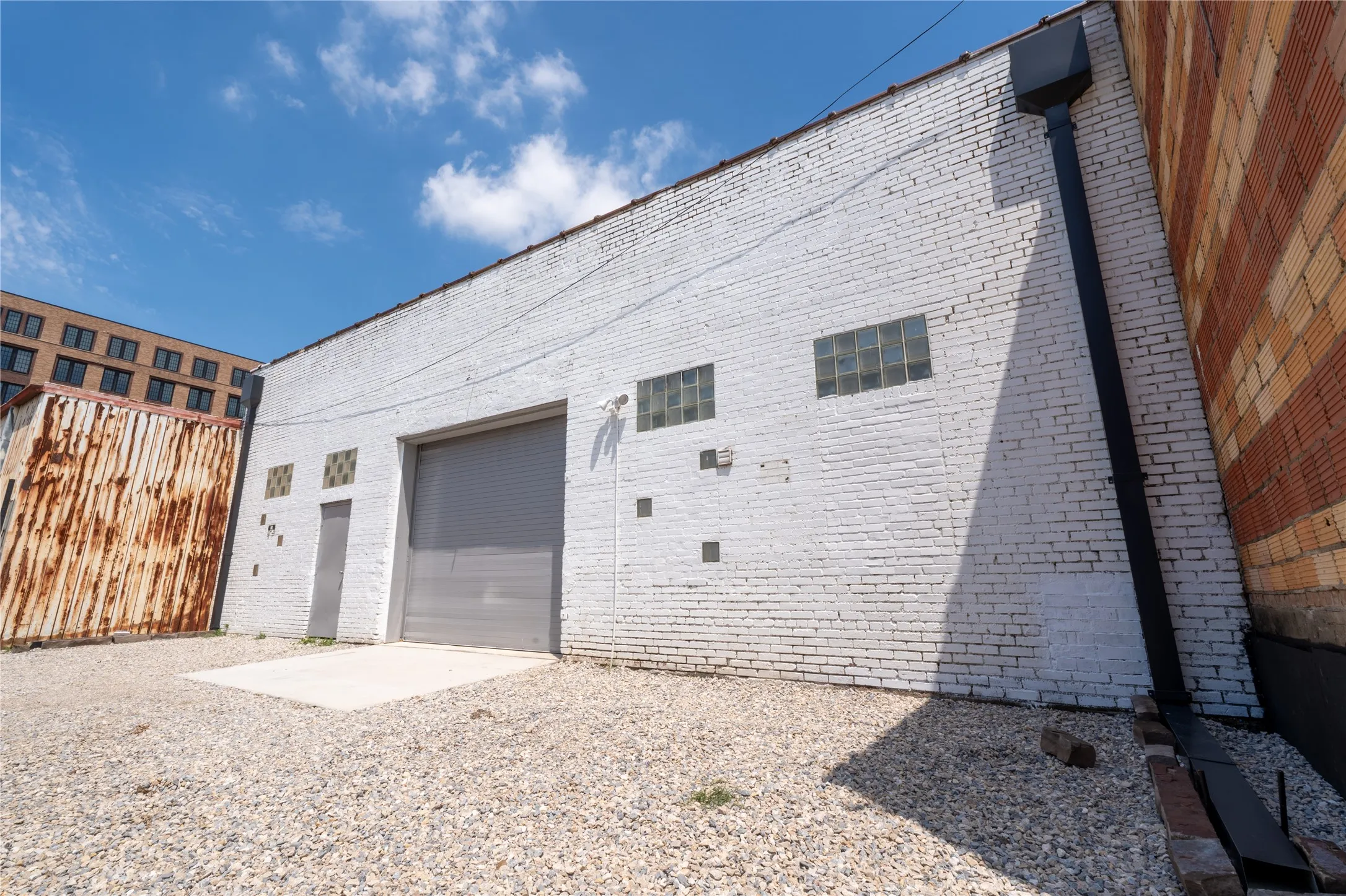 Painted brick exterior featuring a roll-up loading door, pedestrian door, glass block windows, and an external drainage downspout