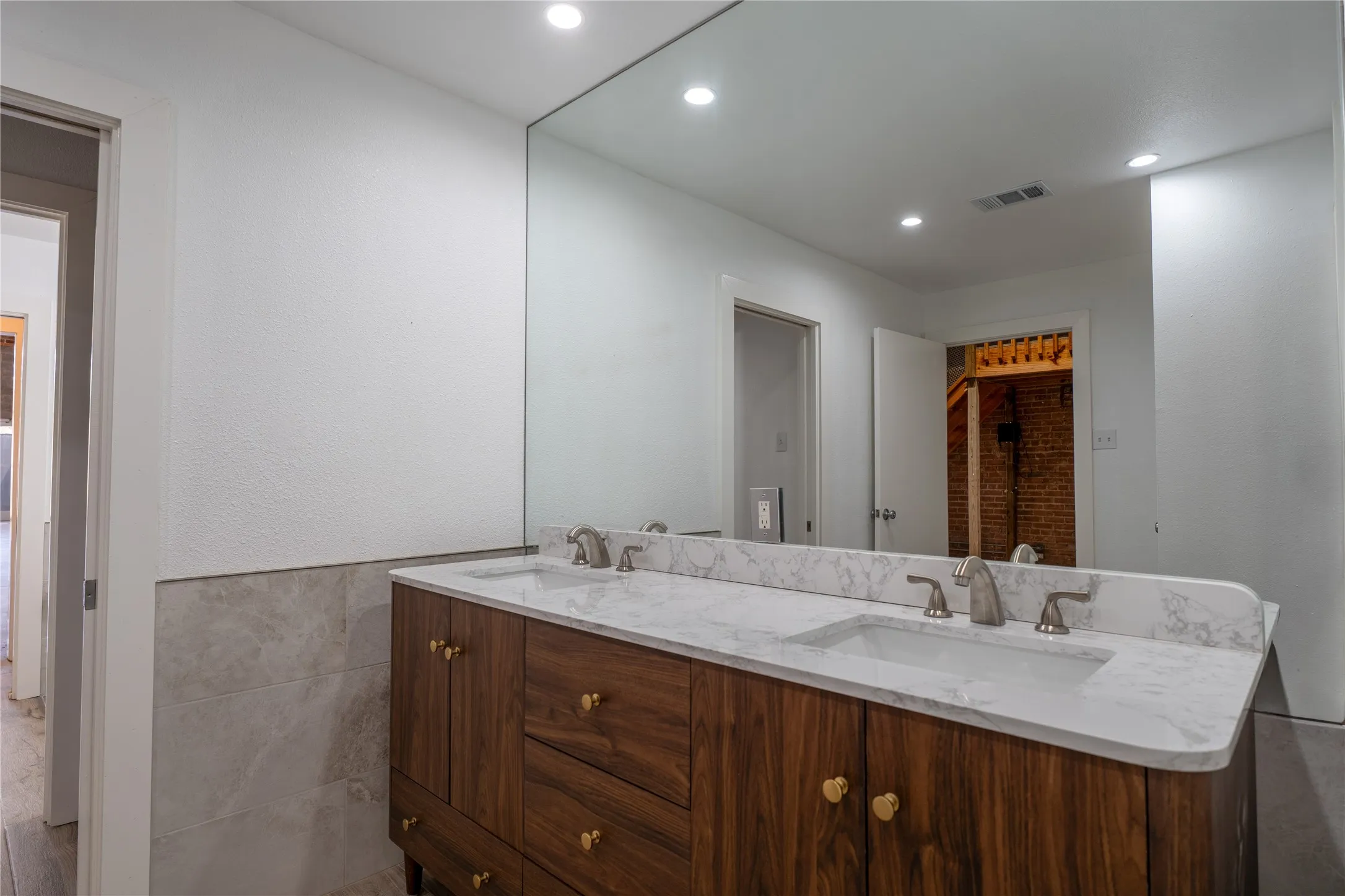 Dual-sink vanity with wood-finish cabinetry, stone-composite countertop, full-width wall mirror, and recessed lighting