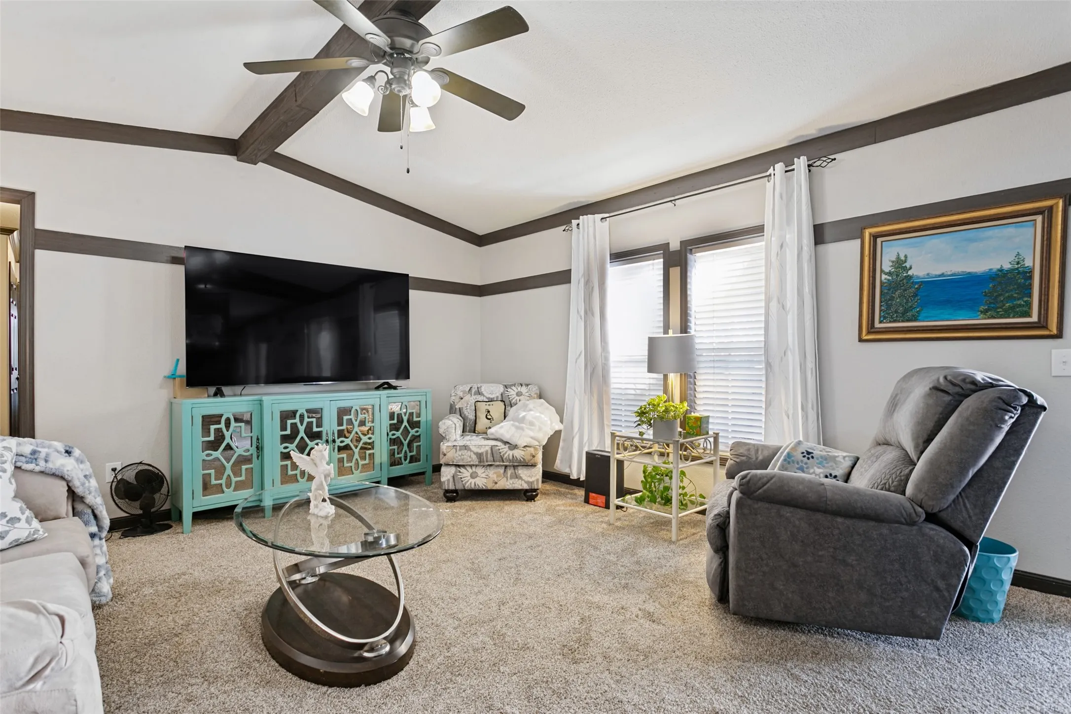 Living area featuring vaulted ceilings, exposed decorative ceiling beam, and wall-mounted ceiling fan with integrated lighting