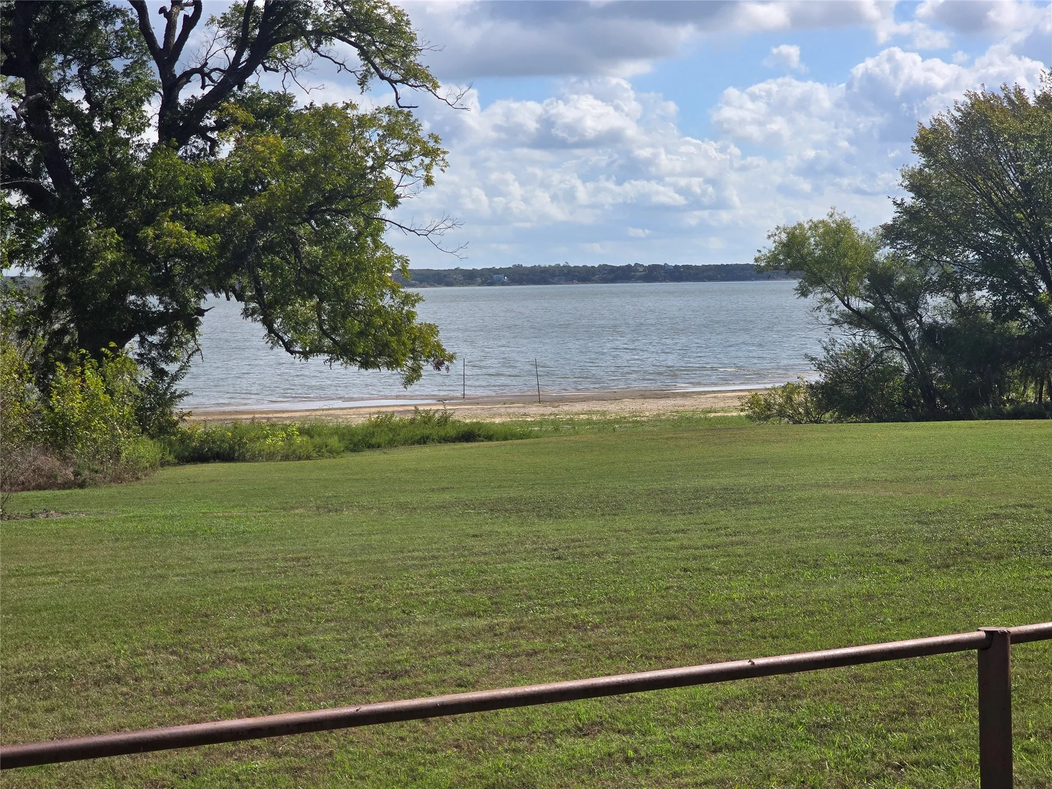 Waterfront lot featuring a grass lawn, sand shoreline, and mature trees