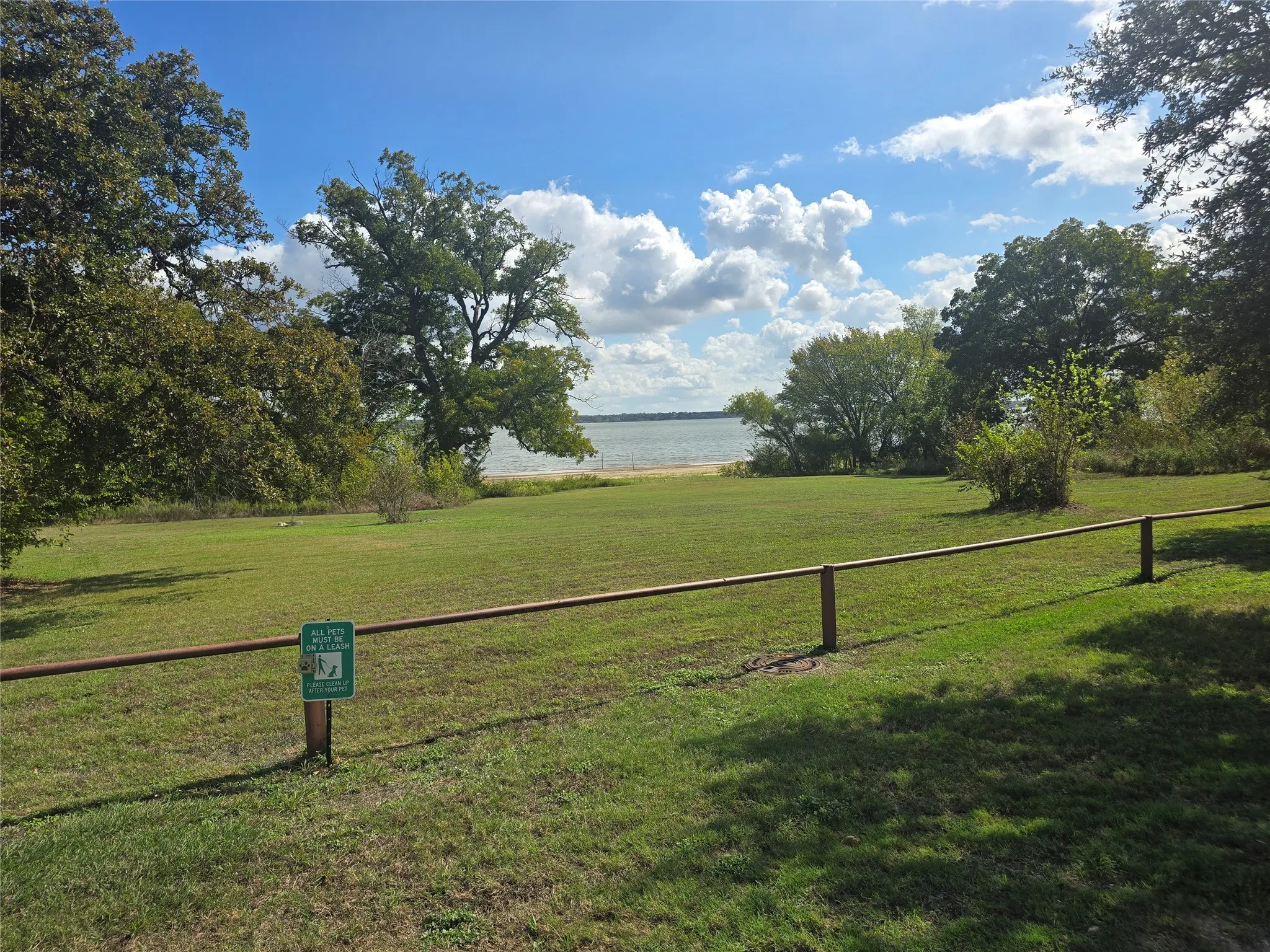 Expansive grassy lot featuring mature trees, a perimeter rail fence, and direct waterfront access