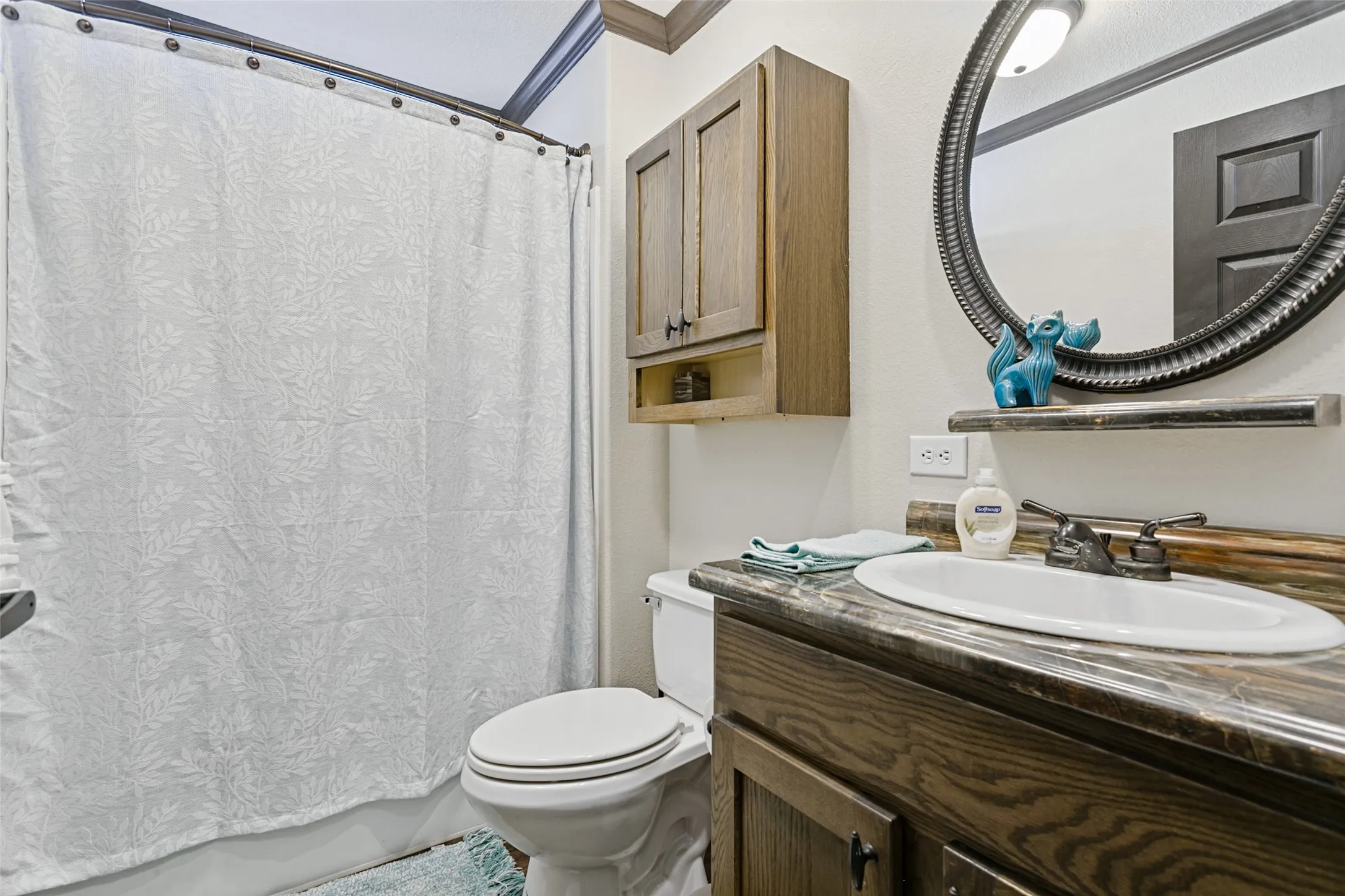 Bathroom vanity with a stone-finish countertop, oval drop-in sink, dark wood-finish cabinetry, wall-mounted storage cabinet, and a circular decorative mirror
