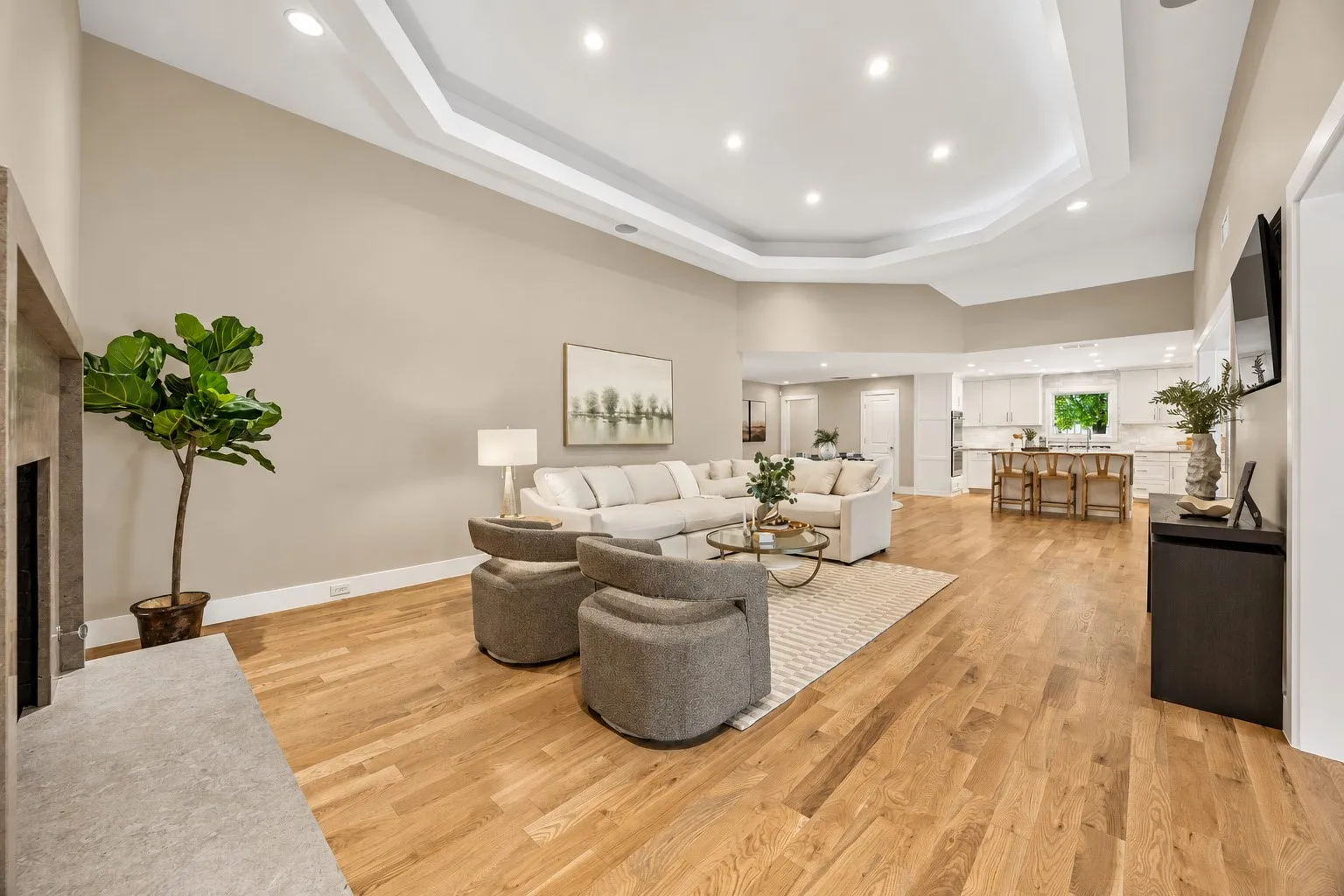 Vaulted tray ceiling with recessed lighting, concrete-surround fireplace, and solid oak flooring