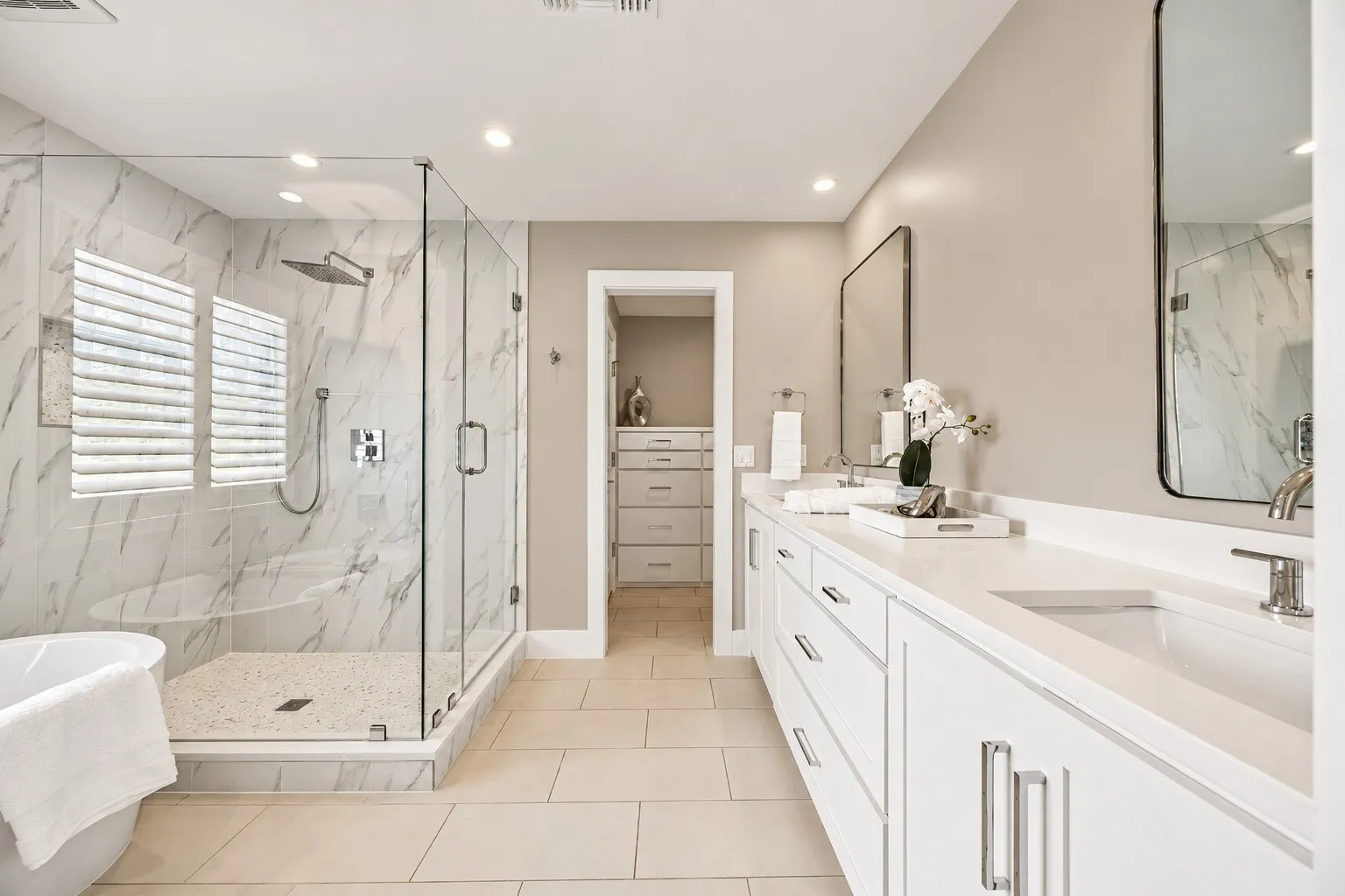 Dual-sink vanity with glass-enclosed walk-in shower, tile surround soaking tub, separate toilet space, two custom walk in closets, and magsafe hidden space