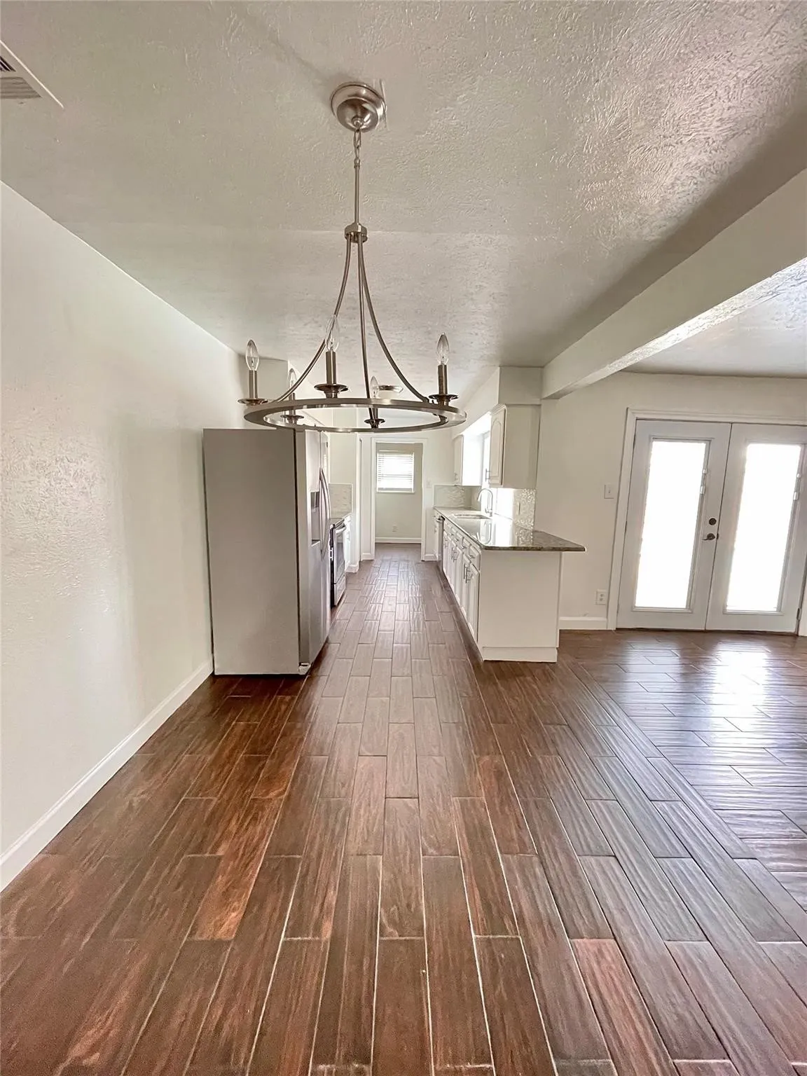 Wood-finish flooring, white cabinetry, neutral stone-finish countertops, stainless steel refrigerator, and a circular brushed-metal chandelier