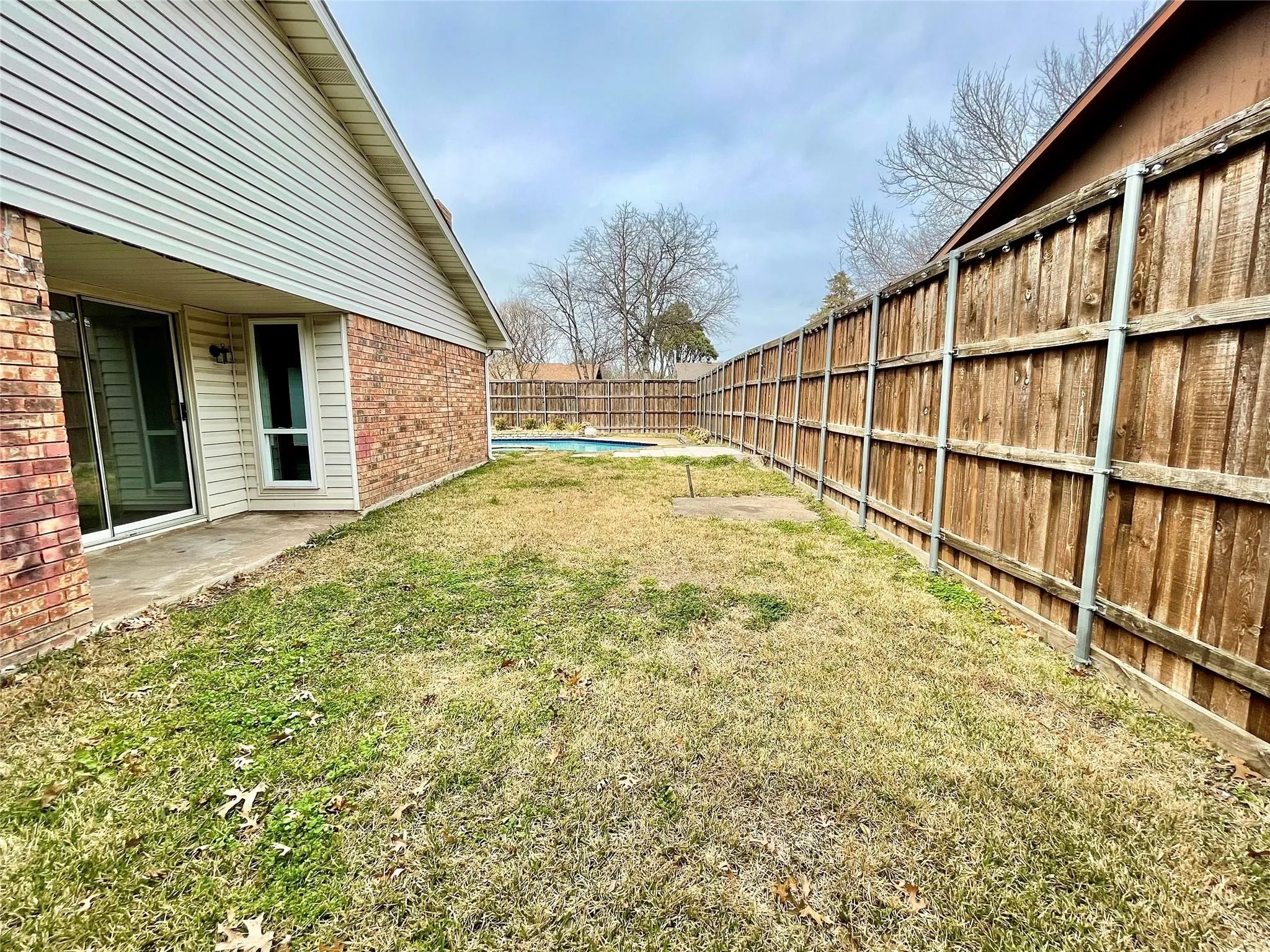 Backyard featuring a concrete patio, brick and siding exterior, inground swimming pool, and full-height wood privacy fencing