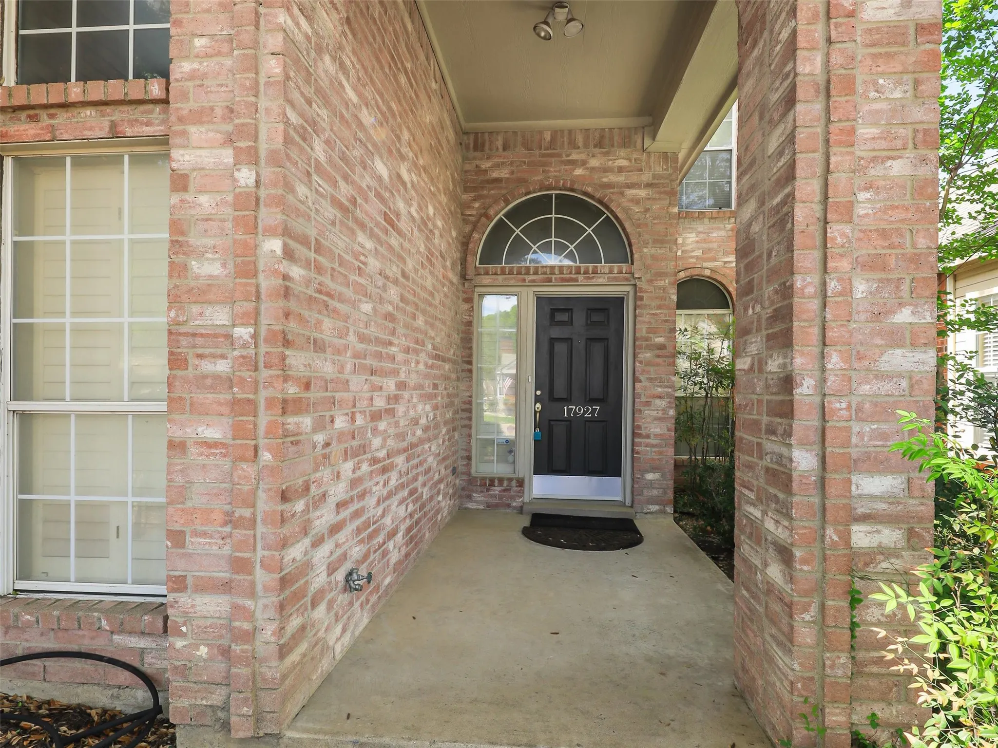 Brick exterior entryway featuring a covered porch, an arched transom window, and a paneled front door with a metal kick plate