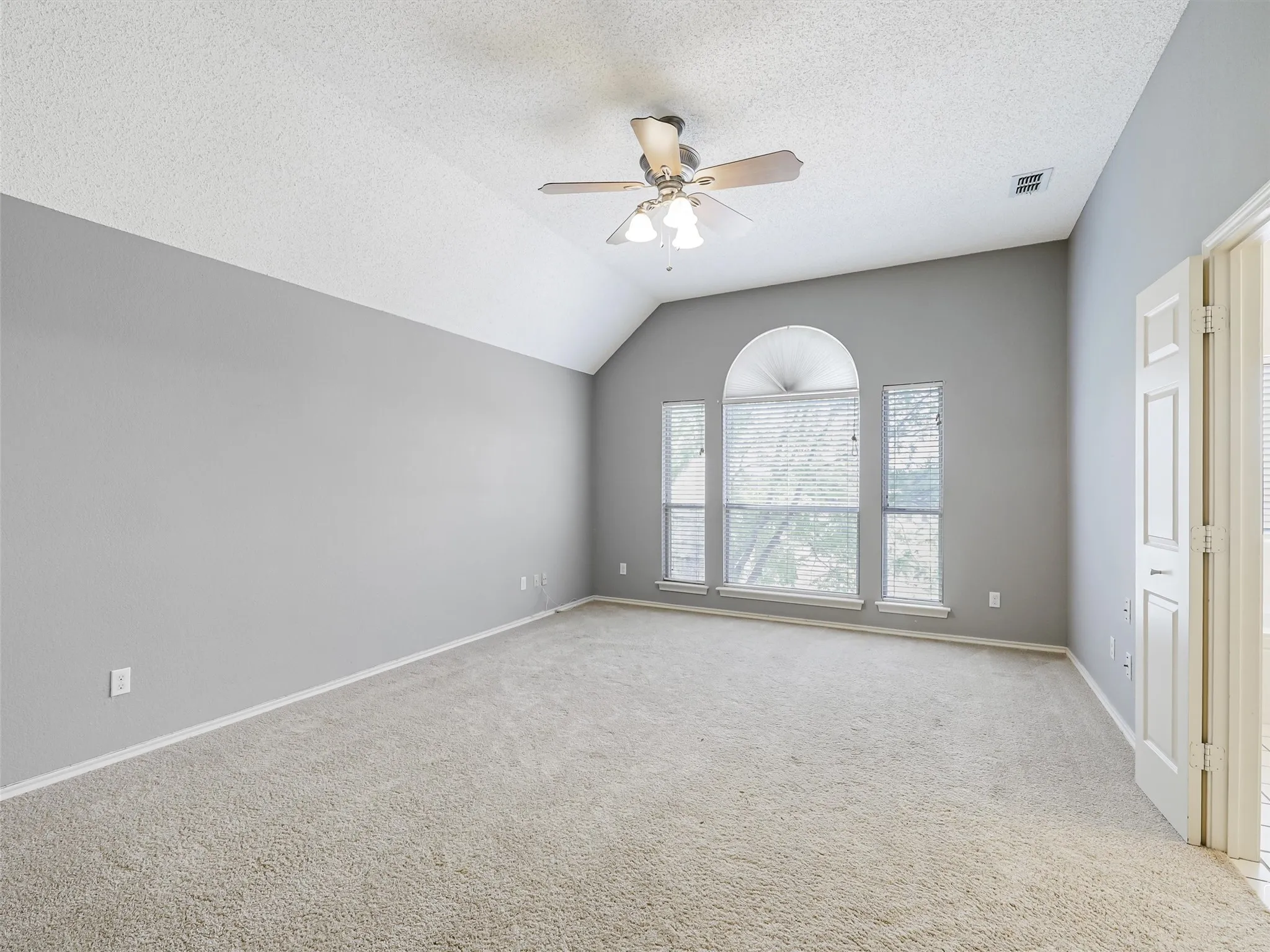 Vaulted ceilings with a ceiling fan, carpeted flooring, and a multi-pane window configuration featuring an arched transom