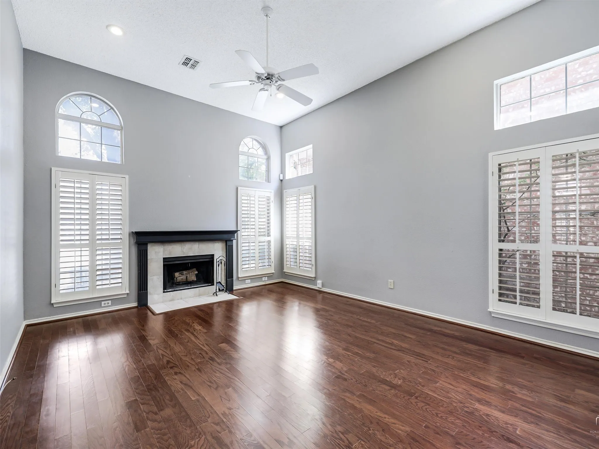 Vaulted ceilings, wood-finish flooring, fireplace with a tile surround, shutter-style window coverings, and arched windows