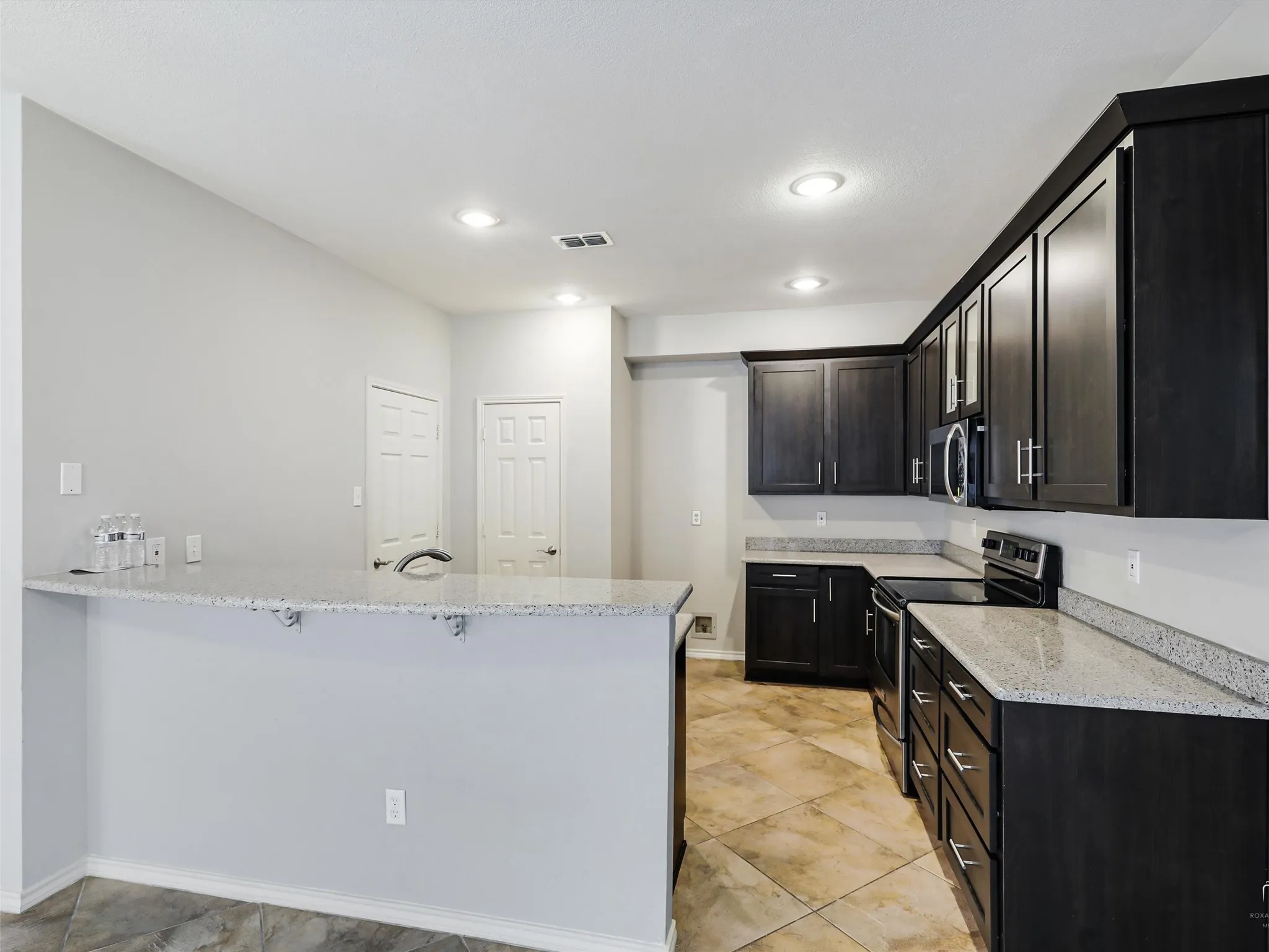 Kitchen featuring dark wood-finish cabinetry, speckled solid-surface countertops, a breakfast bar, tile flooring, and recessed lighting