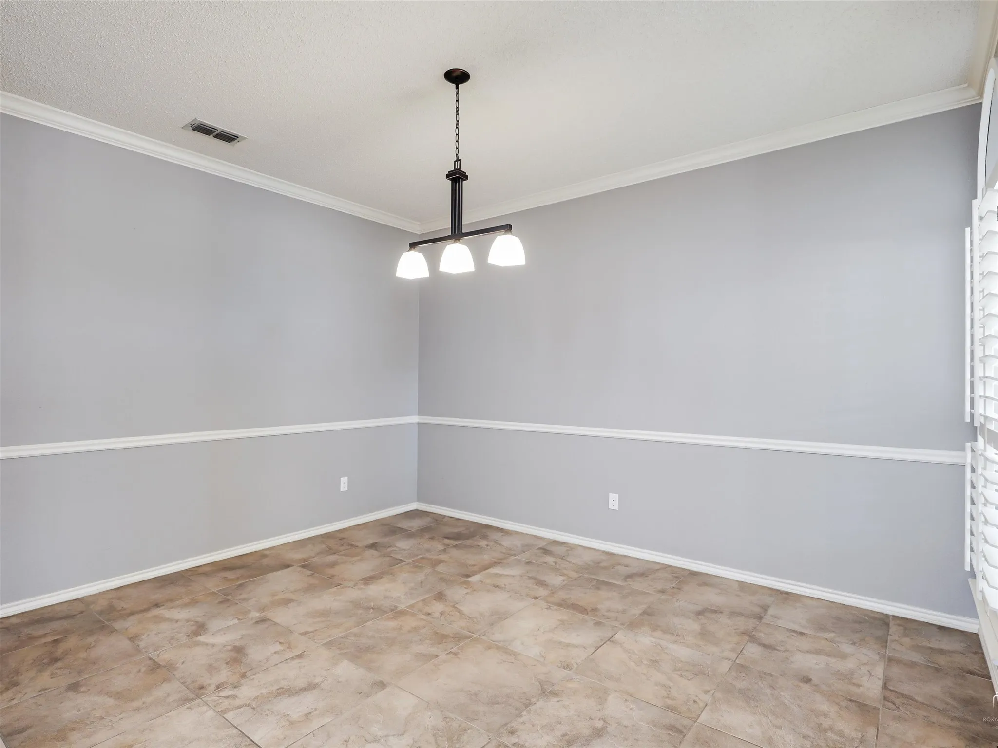Interior room featuring tile flooring, neutral wall paint with white chair rail molding, and a three-light chandelier with a matte finish