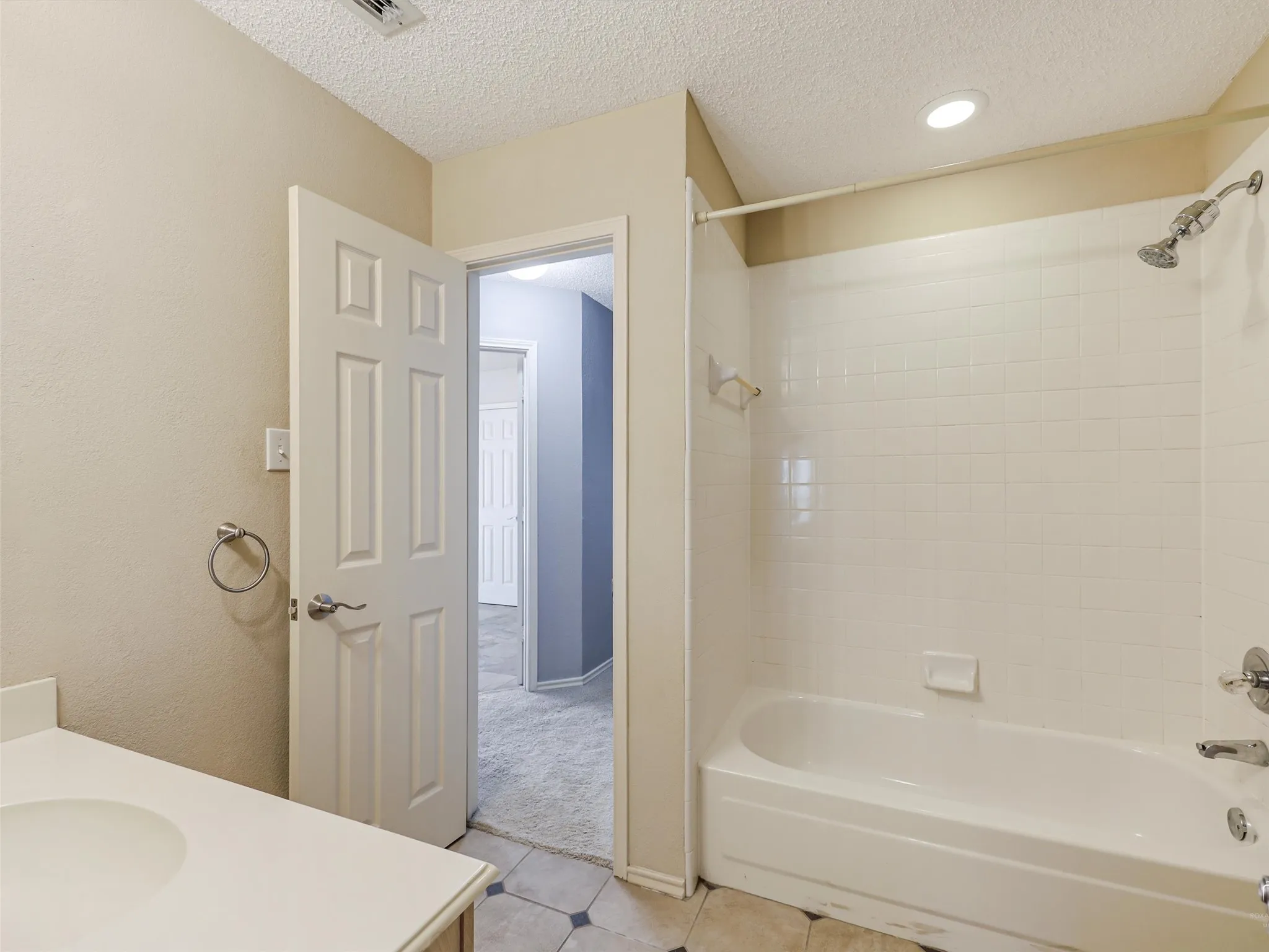 Bathroom featuring a tub-shower combination with white tile surround, recessed lighting, and a single-basin vanity