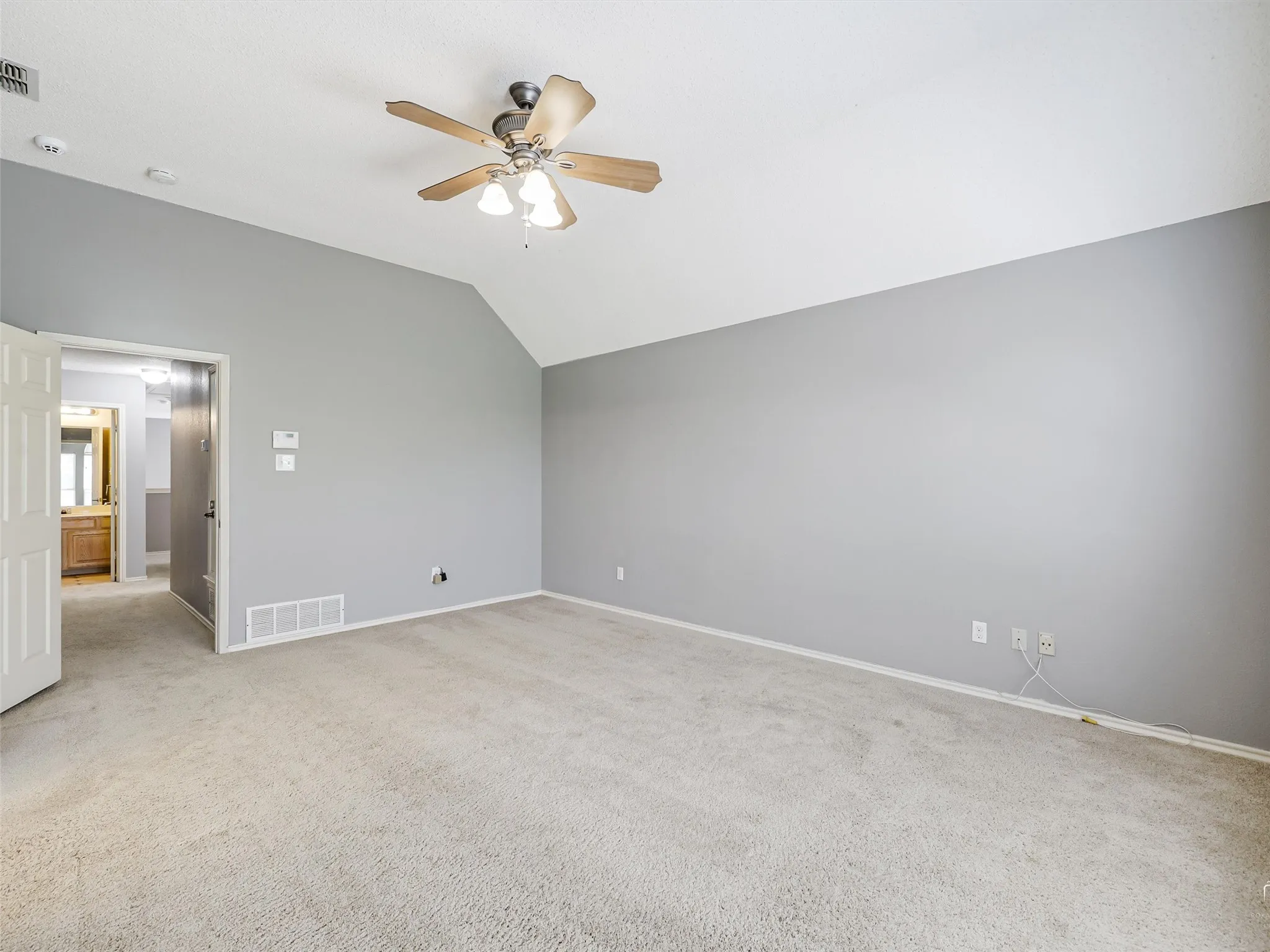 Spacious room featuring vaulted ceilings, neutral wall tones, wall-to-wall carpeting, and a ceiling fan with integrated light fixture