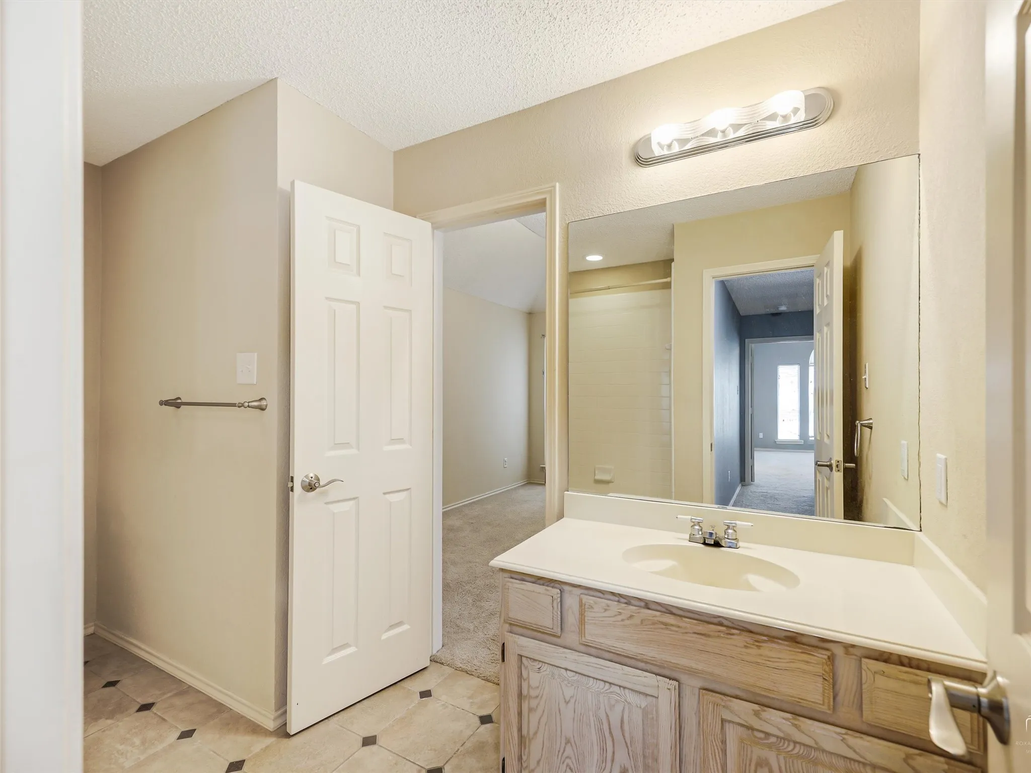 Bathroom featuring a wood-finish vanity with an integrated basin, a large wall-mounted mirror, overhead vanity lighting, and ceramic tile flooring with decorative inlay accents