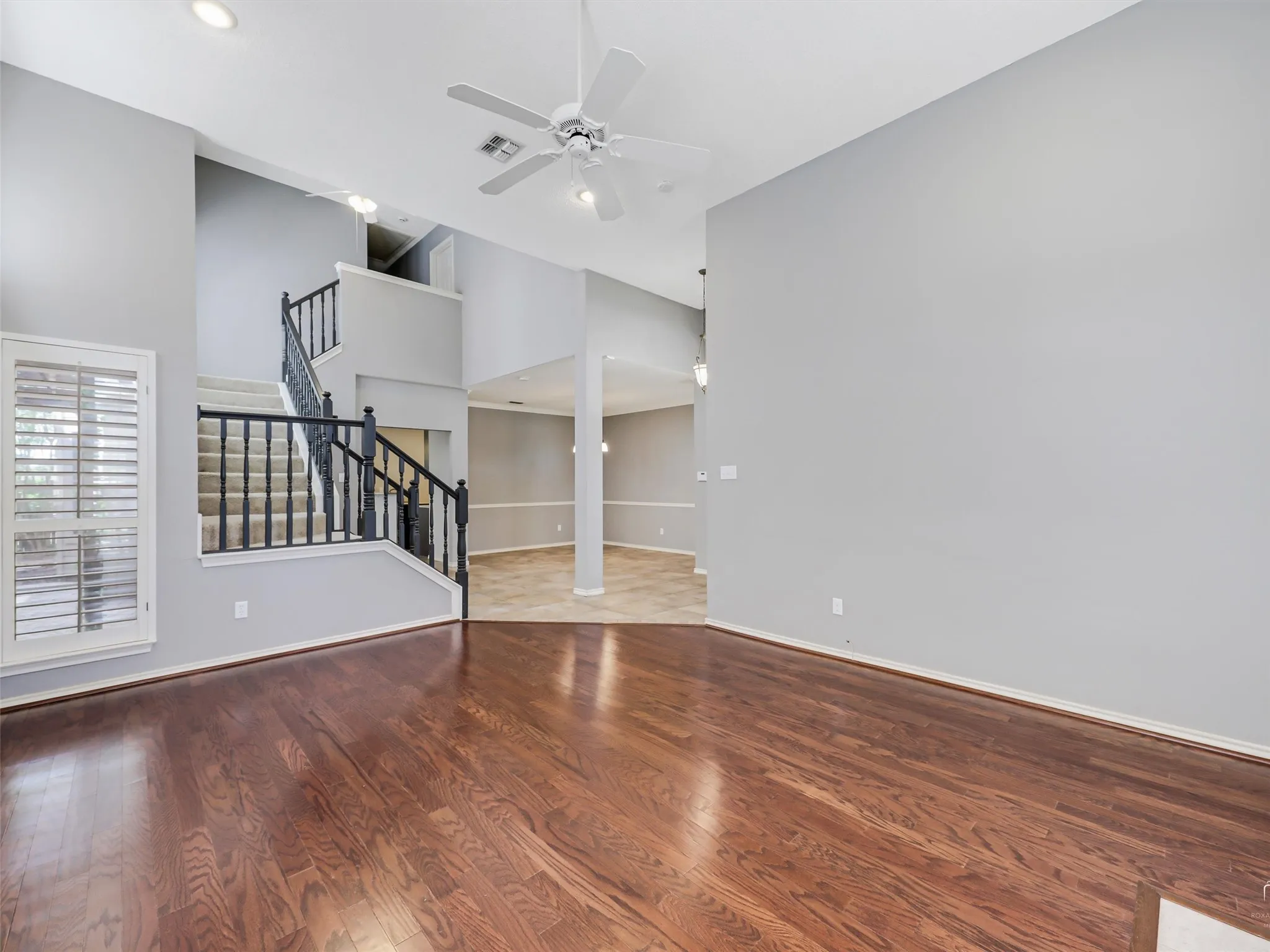 High-ceiling interior featuring wood-finish flooring, a staircase with black metal balusters, shuttered windows, and recessed lighting