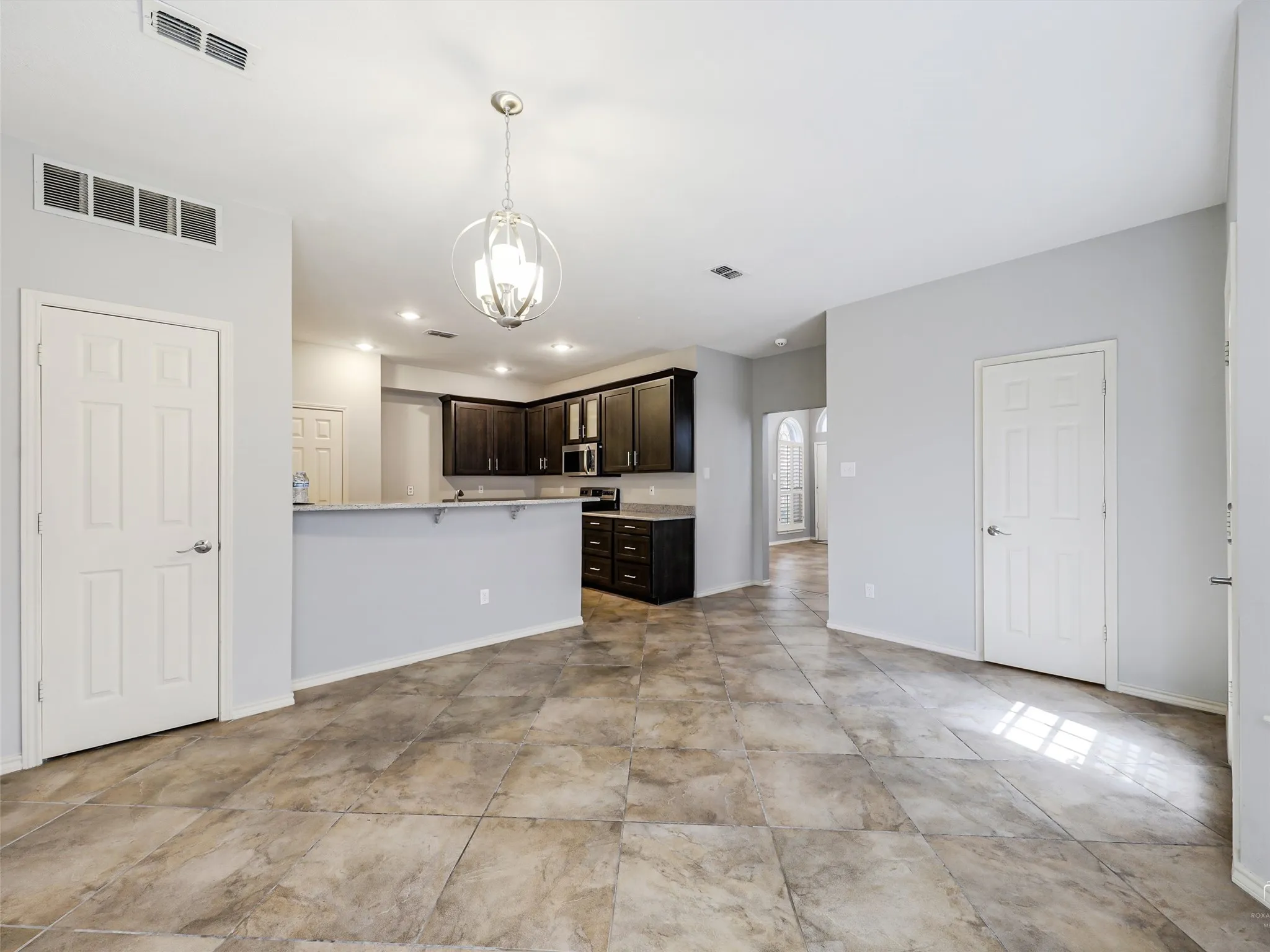 Kitchen featuring dark cabinetry, stone-finish countertops, a tiered breakfast bar, and a brushed nickel pendant light fixture, complemented by tile flooring