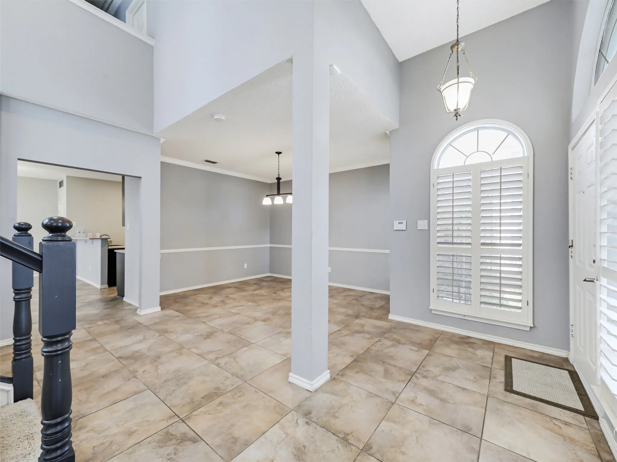 Two-story foyer featuring tile flooring, an arched window with interior plantation shutters, neutral wall tones, chair rail molding, and a suspended metal chandelier