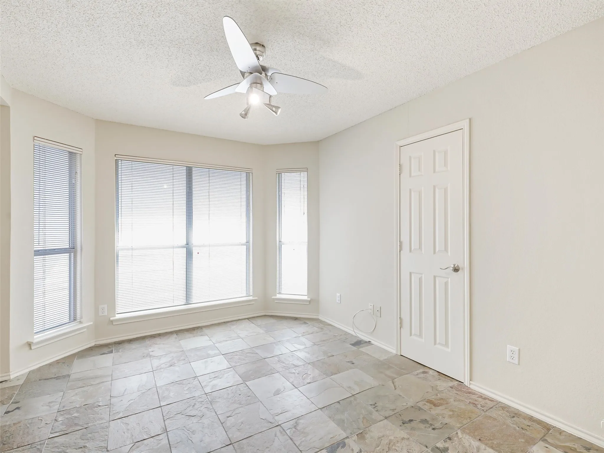 Bay window featuring three paneled windows, ceiling fan with integrated lighting, and stone-tile flooring