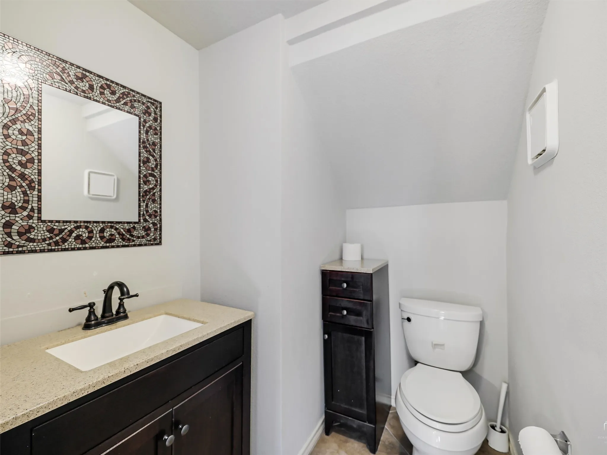 Powder room featuring a dark-toned vanity with a stone-composite countertop, undermount sink, oil-rubbed bronze faucet, and decorative mosaic-tiled wall mirror
