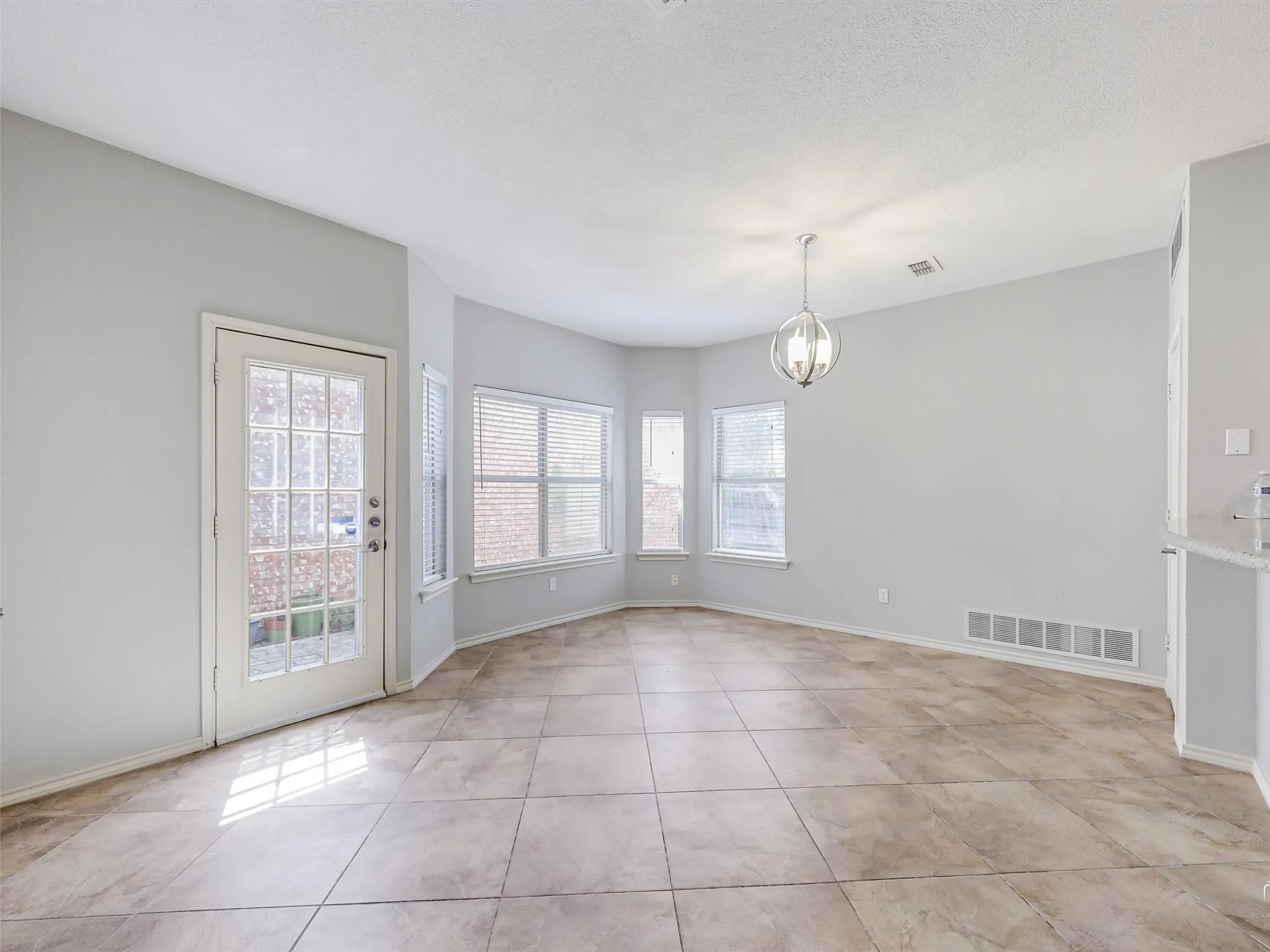 Open-concept area featuring large-format tile flooring, a bay window configuration, a glass-paneled exterior door, and a spherical pendant light fixture