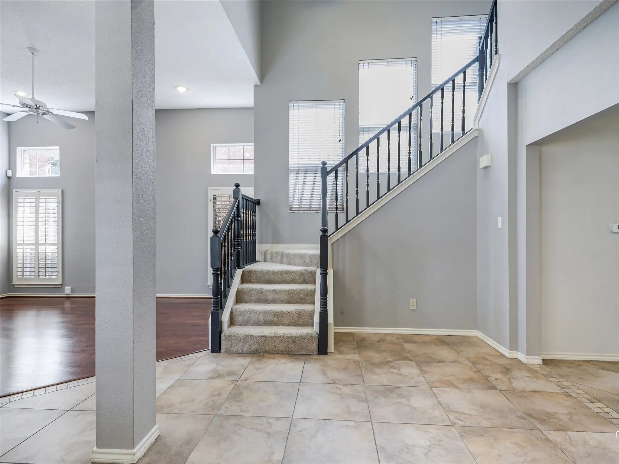 High-ceiling foyer featuring tile flooring, a staircase with a dark wood-finish railing, multi-pane windows, and inset ceiling lighting