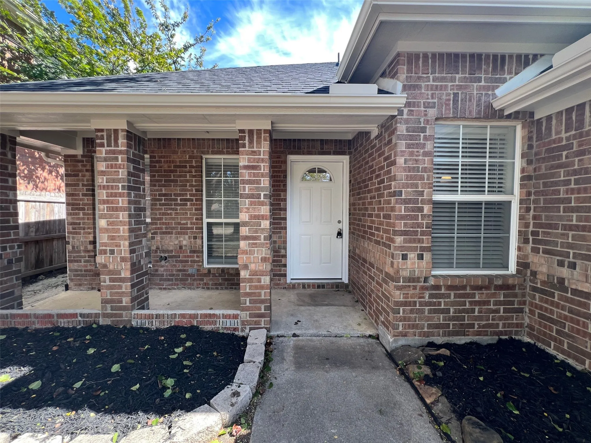 Brick exterior facade with a covered porch, brick-pillar support columns, and concrete walkway