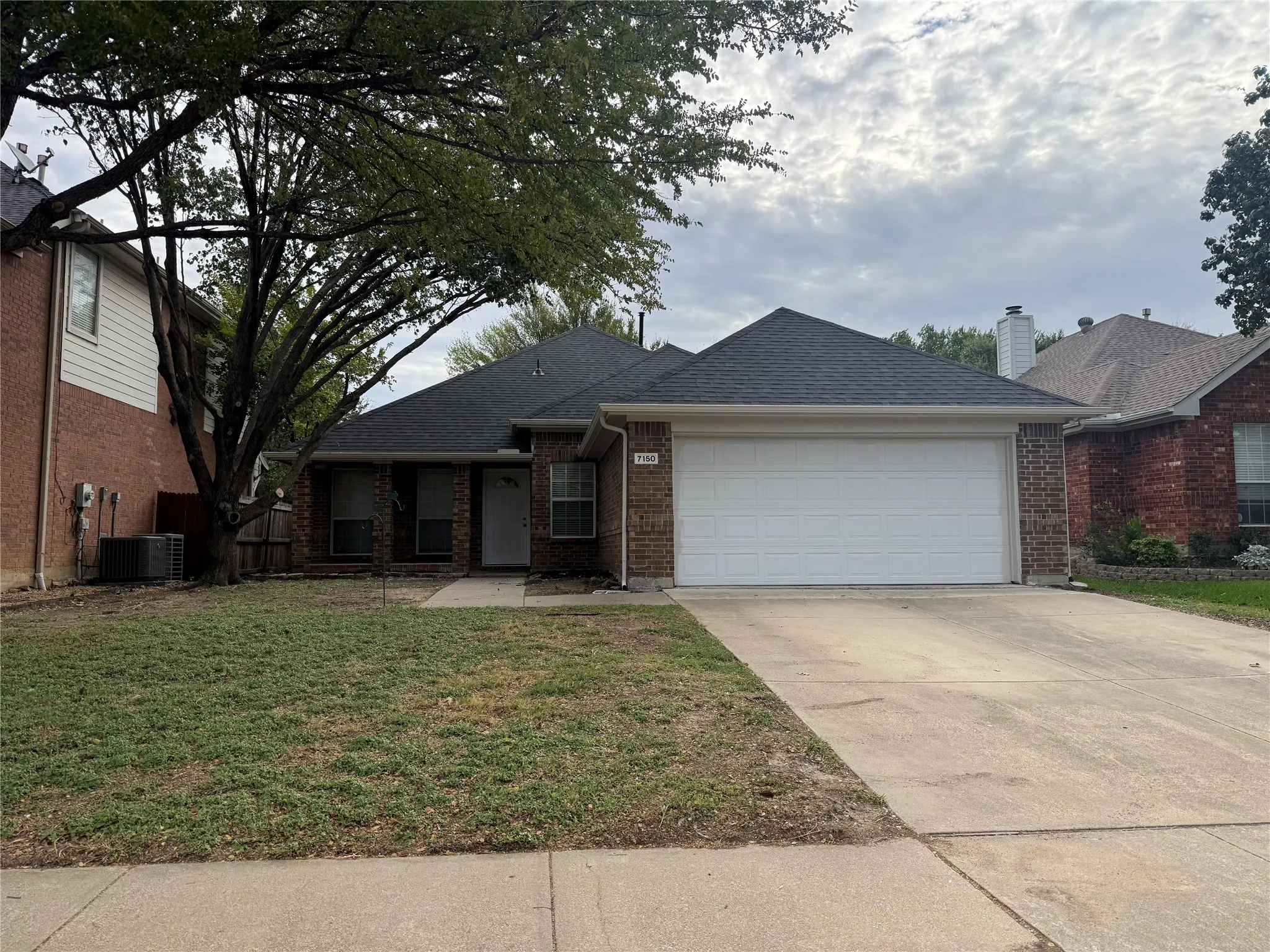 Single-story brick exterior featuring a hip roof, two-car garage, concrete driveway, and mature landscaping