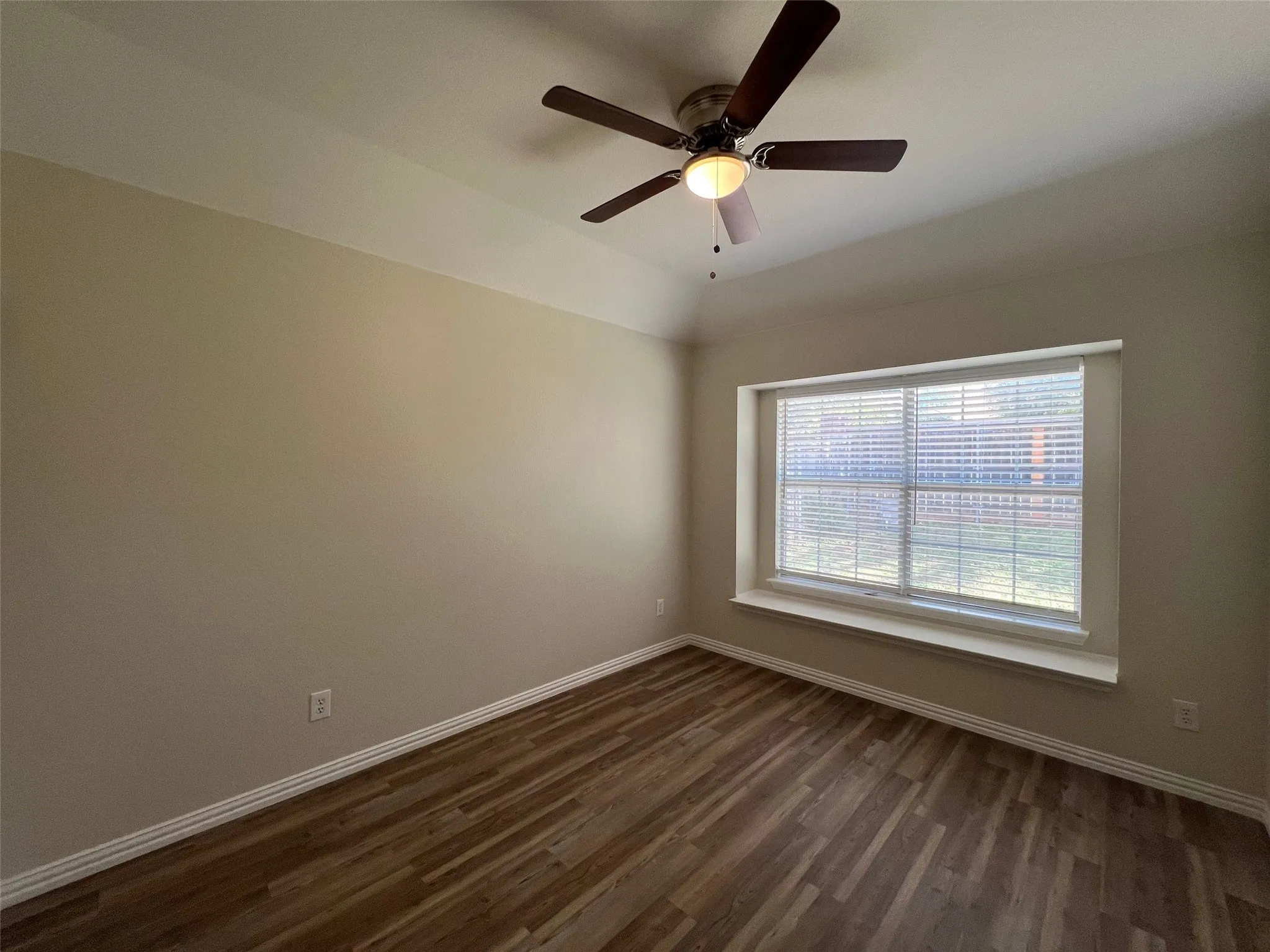 Room featuring wood-finish flooring, a recessed tray ceiling, a central ceiling fan with integrated lighting, and a window seat set into a large recessed window