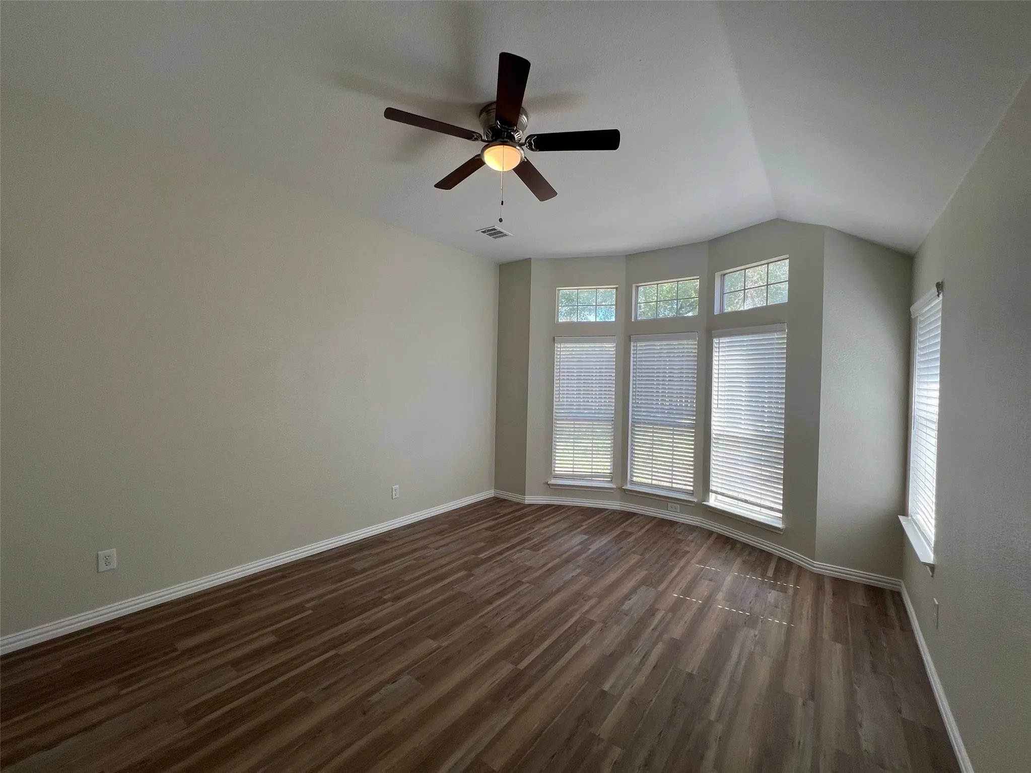 Room featuring vaulted ceilings, wood-finish flooring, a bay window with multiple panes, and a ceiling fan with integrated lighting
