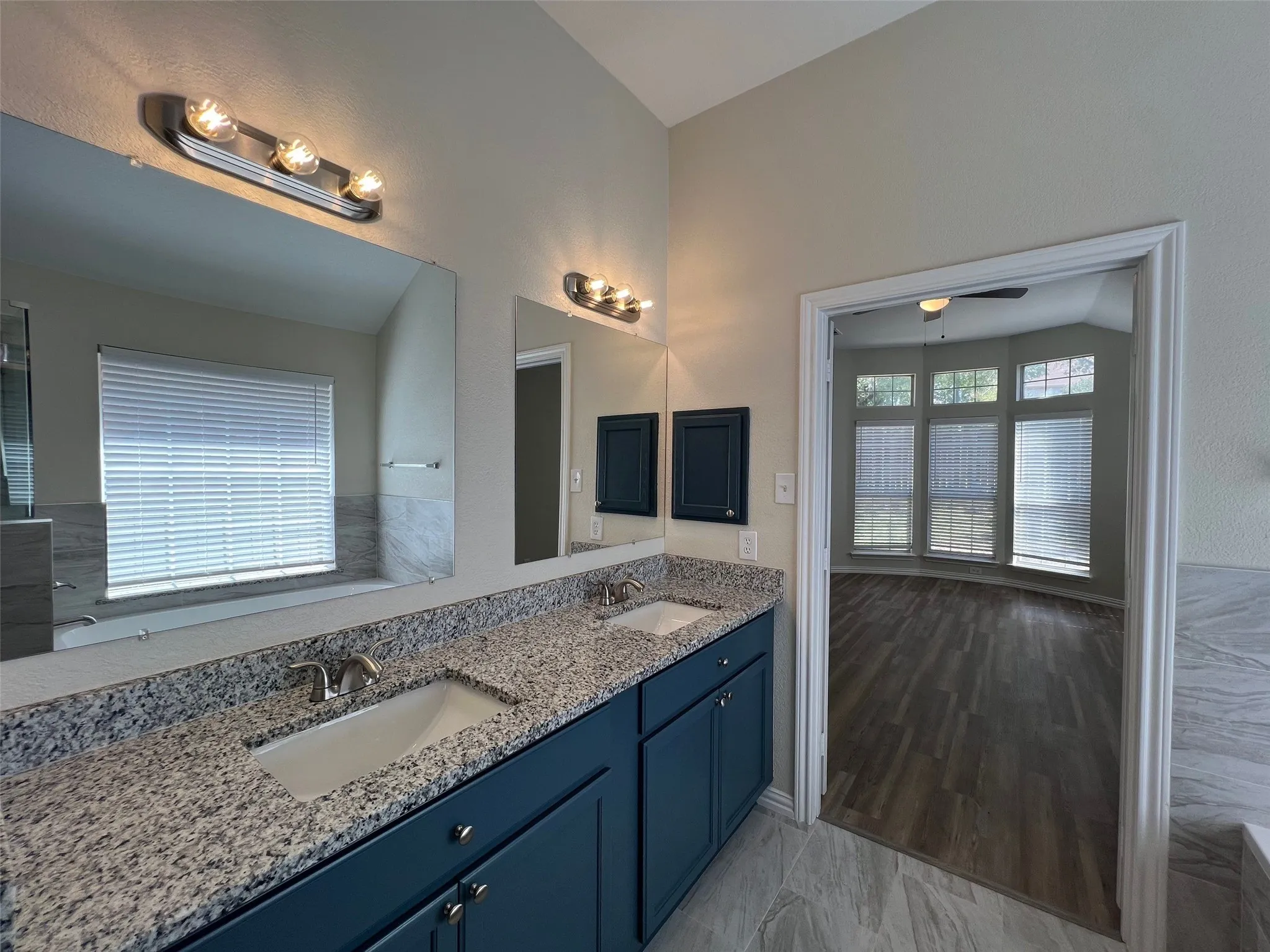 Dual-sink vanity with stone-finish countertop, dark-toned cabinetry, wide-format mirrors, and wall-mounted vanity lighting
