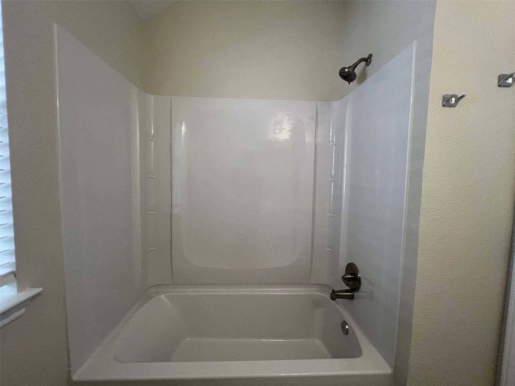 Built-in bathtub with a white surround, featuring a wall-mounted shower head and metallic hardware